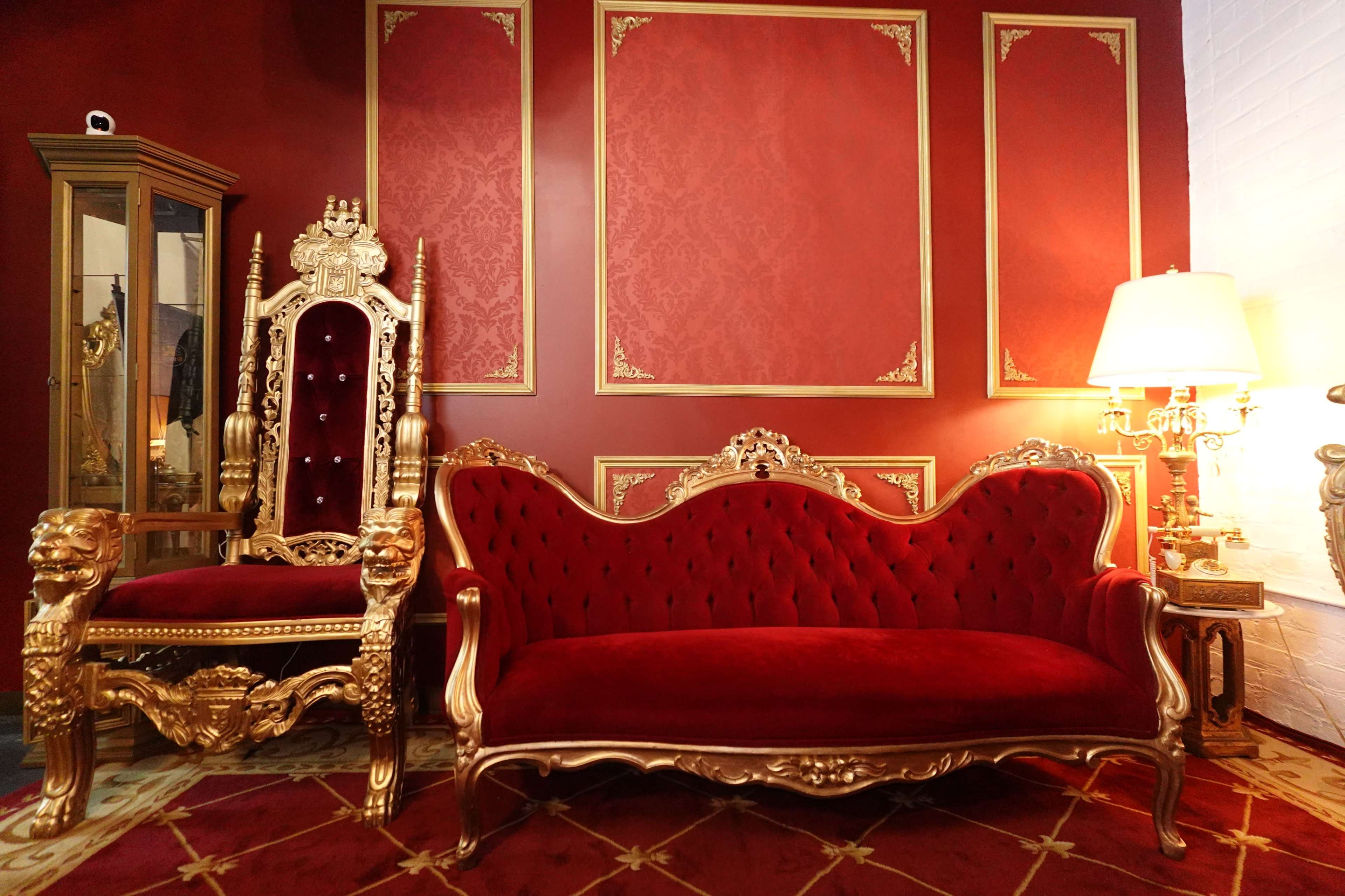 The image features an ornate, red and gold seating area with a luxurious sofa and a grand throne-like chair against a richly colored wall.