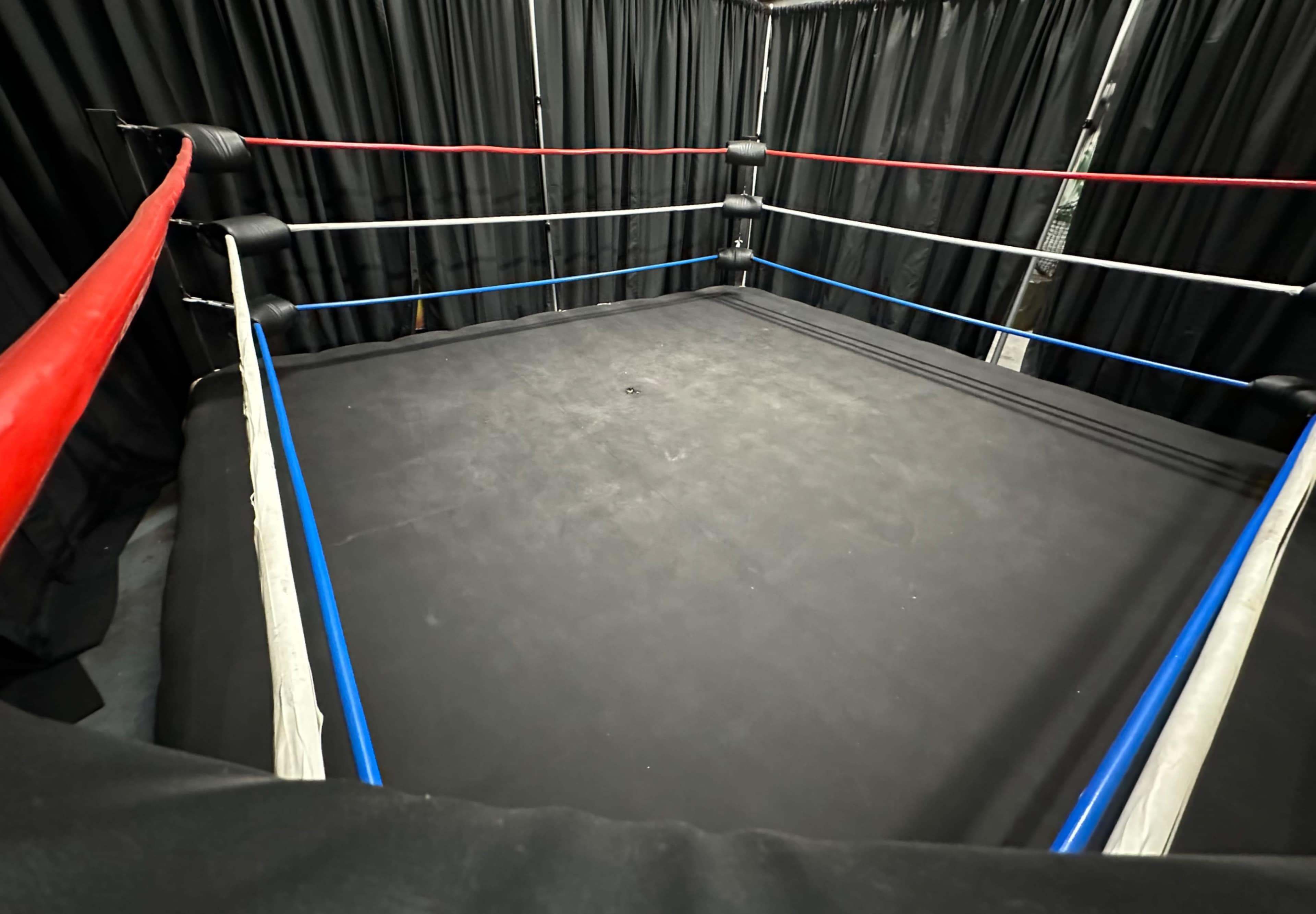An empty boxing ring surrounded by black curtains with red, white, and blue ropes.