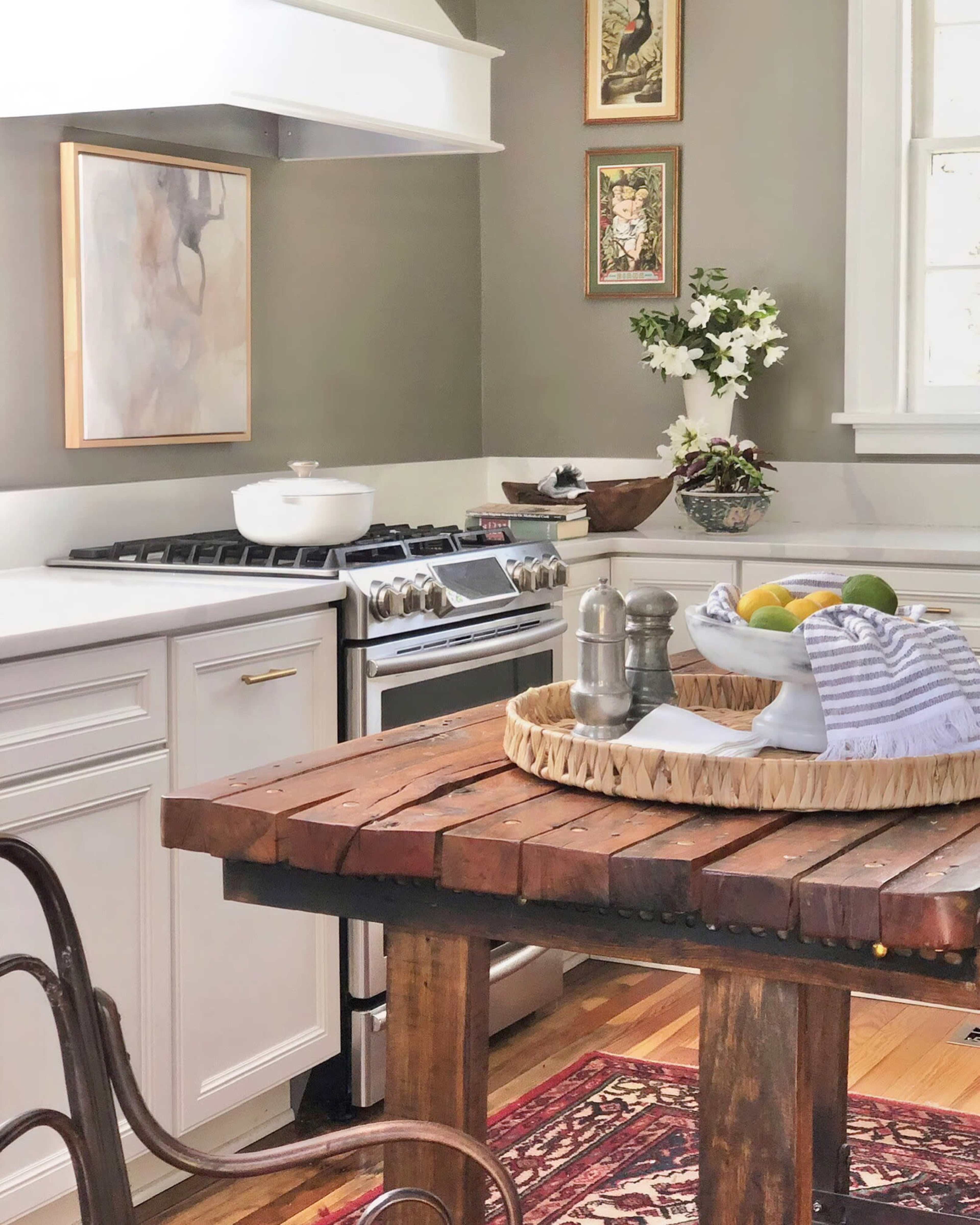 A modern kitchen with a wooden dining table, gas stove, and various kitchen decor, including fruit and flowers.
