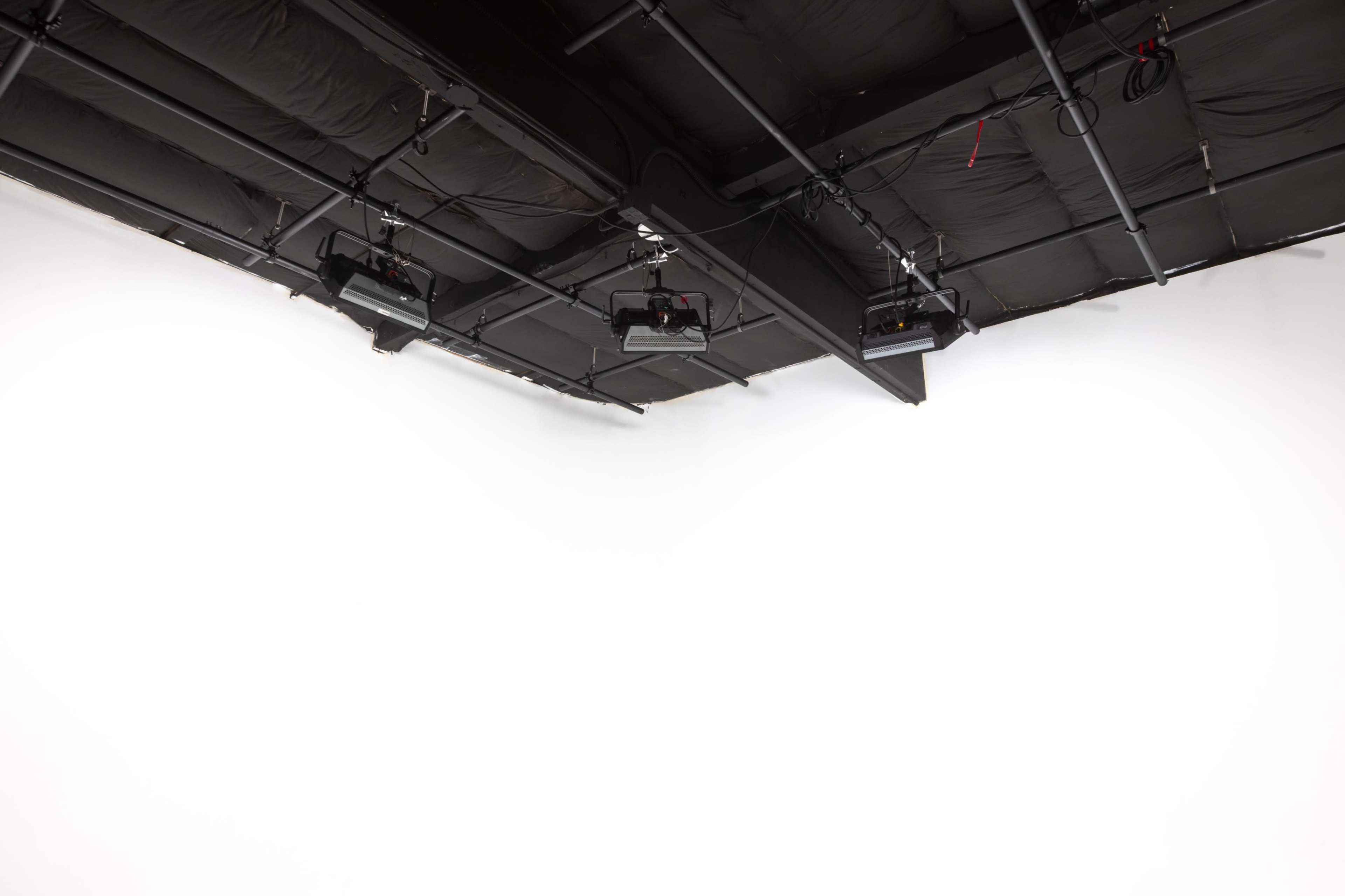 The image shows a studio with a white backdrop and multiple lights mounted on the ceiling.