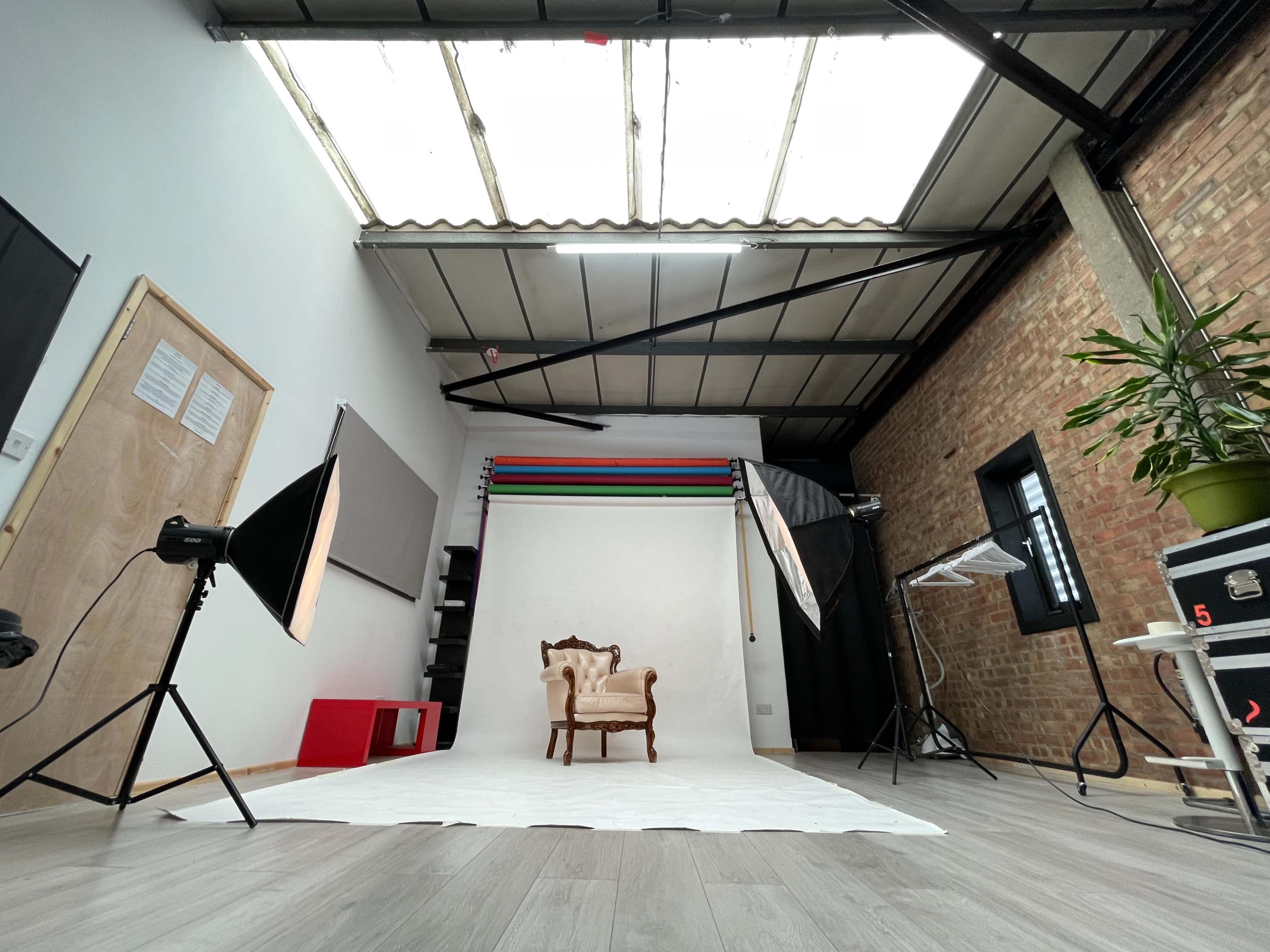 A photography studio with a vintage chair positioned on a white backdrop, surrounded by lighting equipment and a brick wall.
