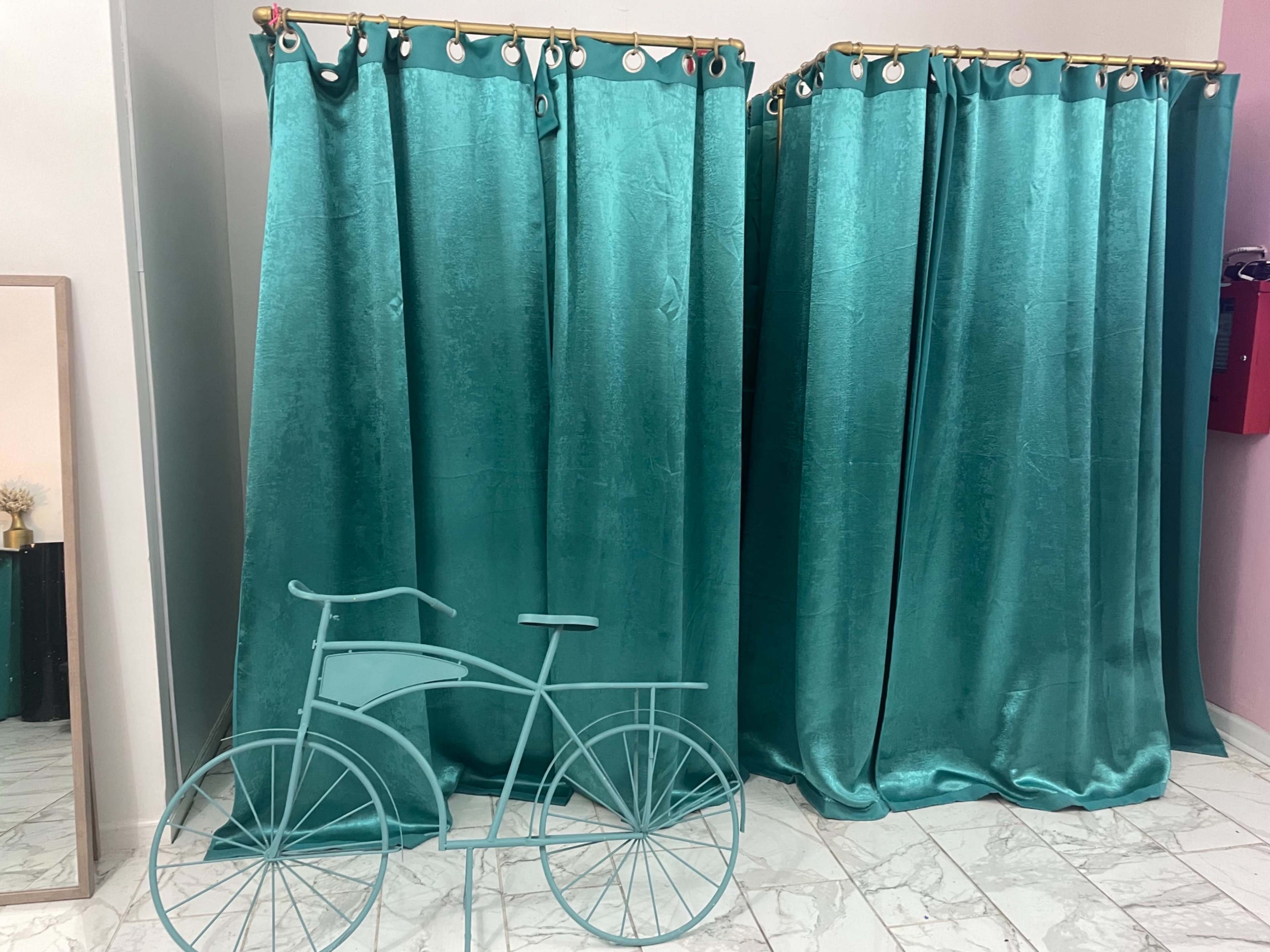 A small area with teal curtains hanging in front of changing rooms and a decorative metal bicycle in front of them.