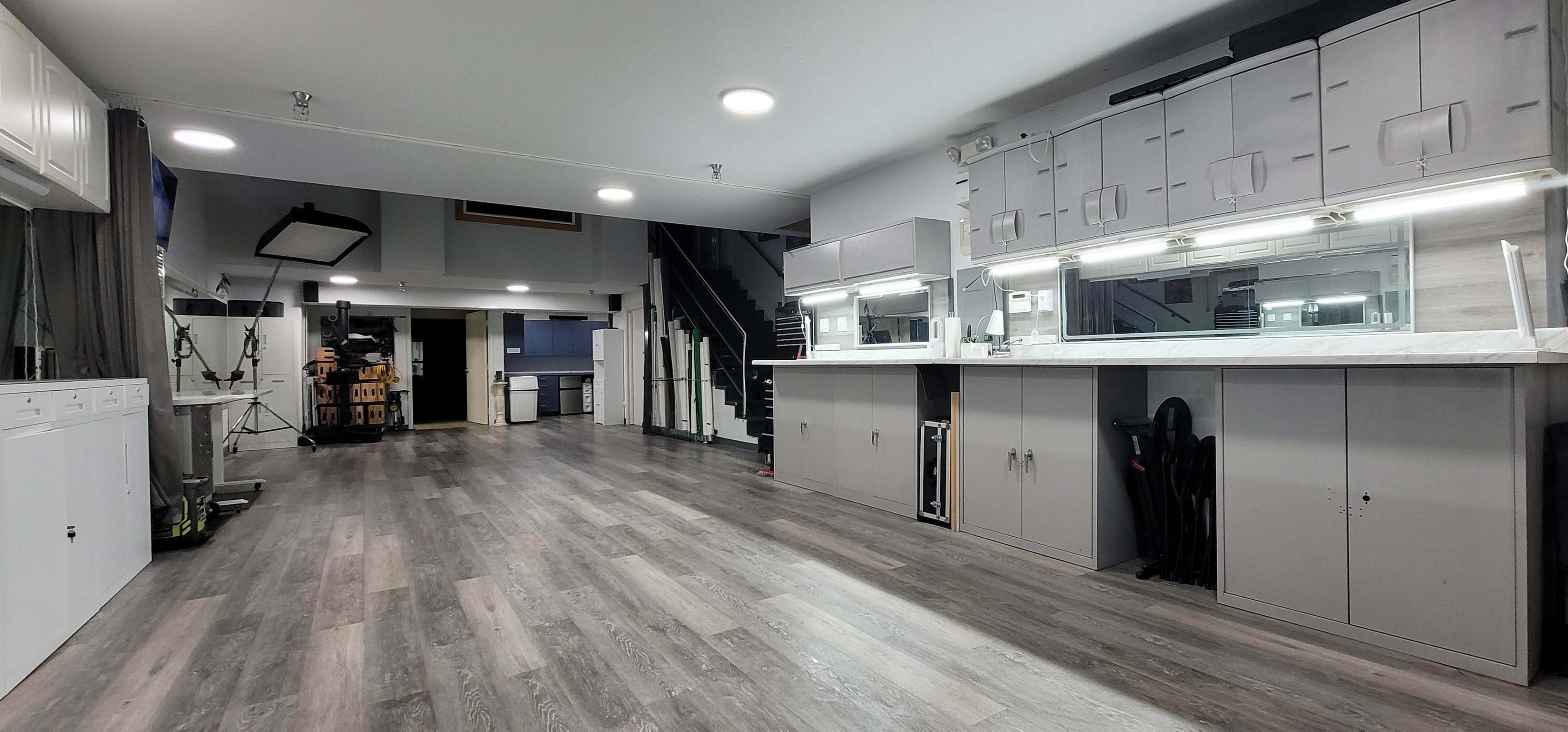 The image shows a spacious, modern interior with a large open area featuring gray flooring, built-in cabinets, sinks, and a staircase in the background.
