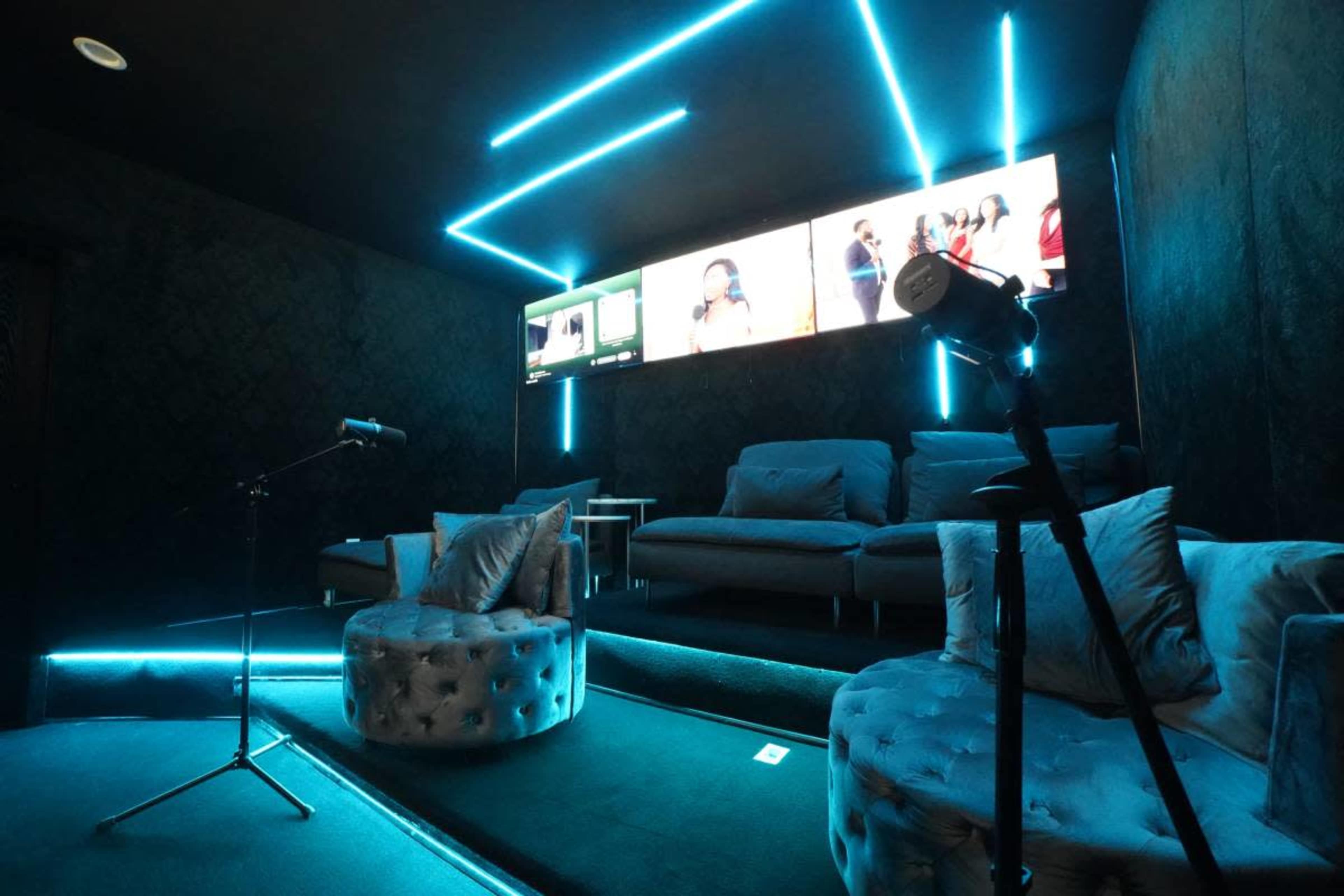 The image shows a modern home theater room with plush seating, illuminated by blue LED strip lights, and featuring a large screen displaying content.