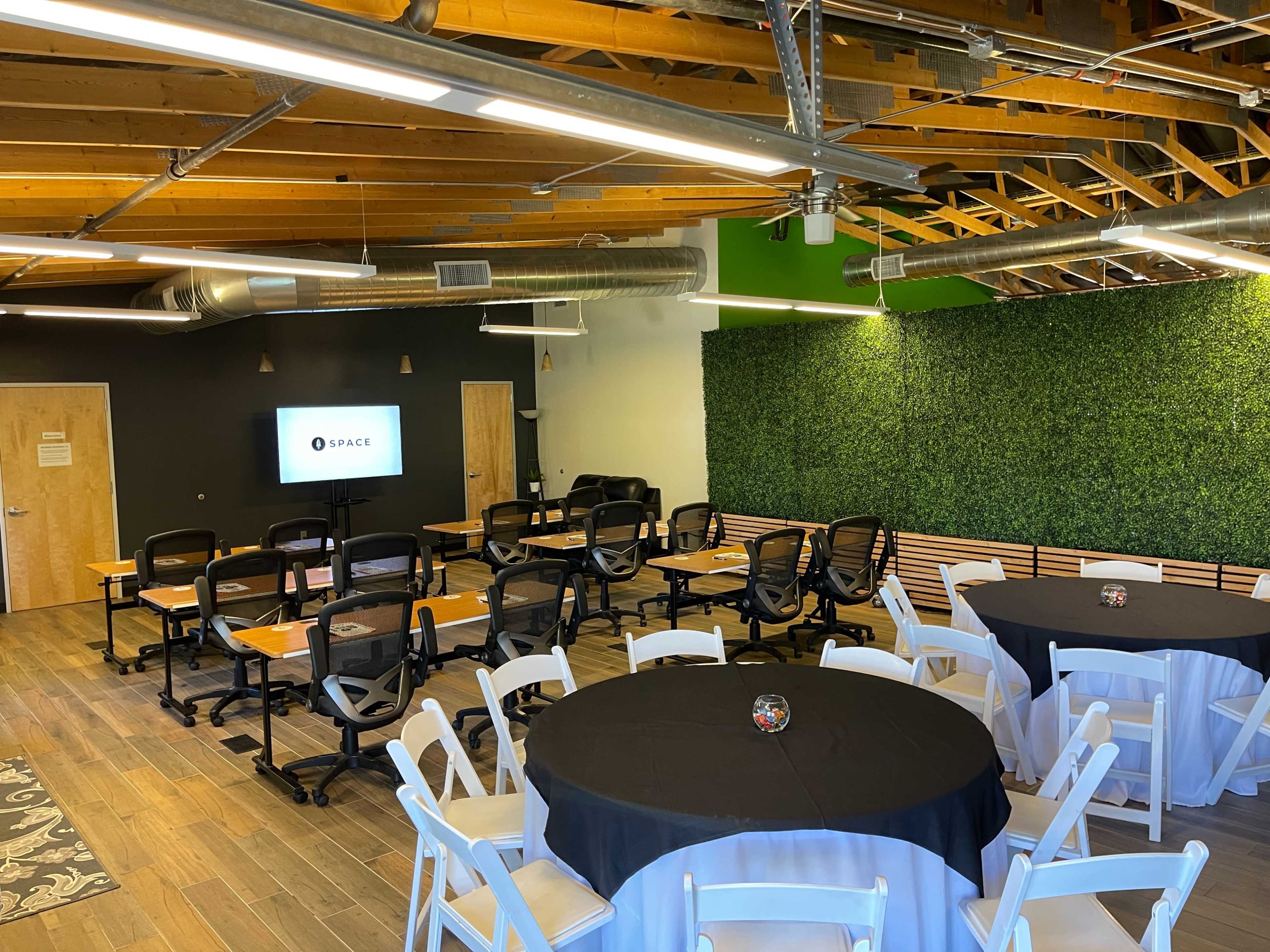 A modern meeting room with rows of black chairs and tables set up, alongside a green wall and a screen displaying the word "SPACE."
