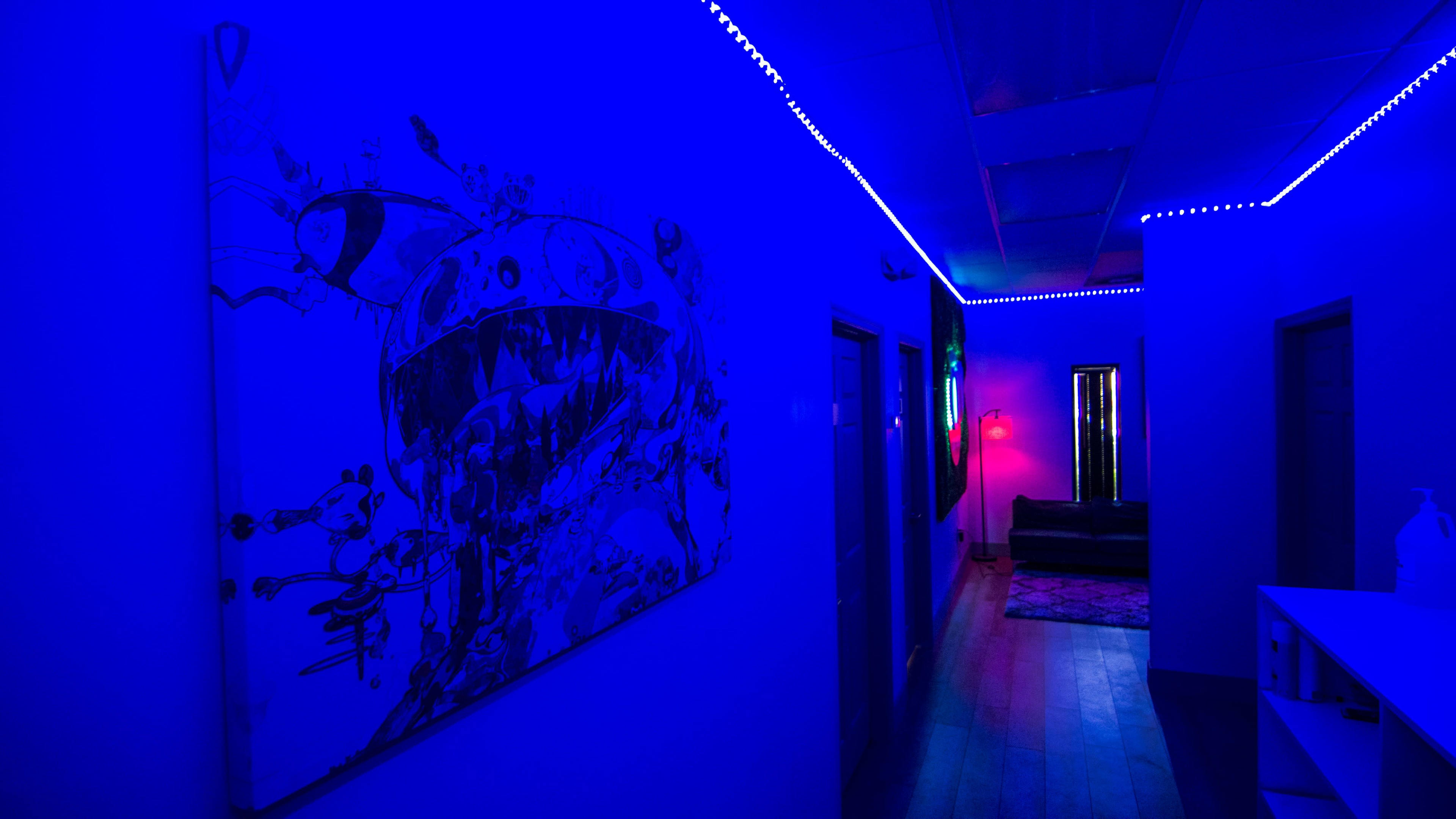 A hallway features blue lighting, an artwork of a monster on the wall, and a sofa at the far end.