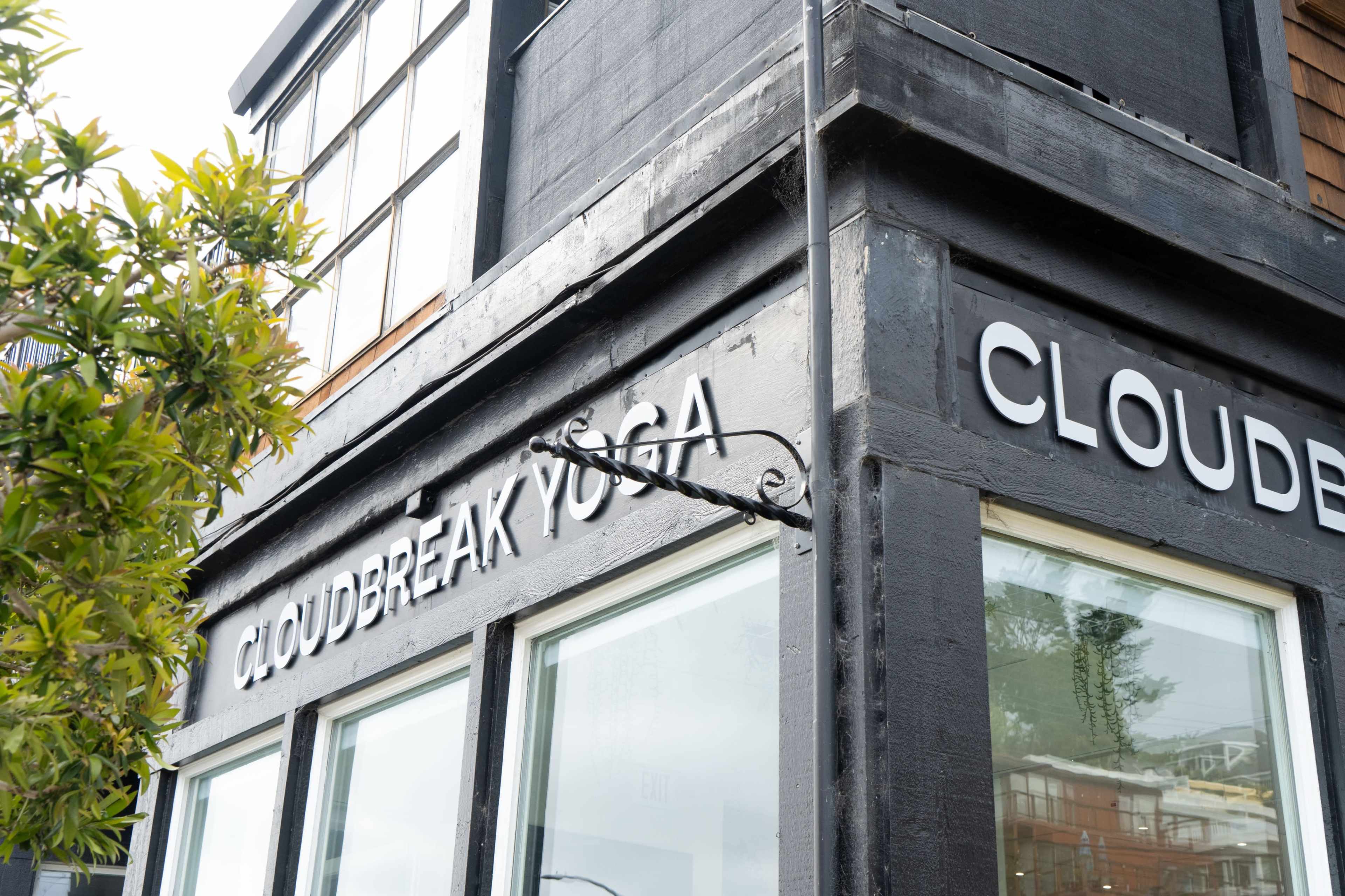The exterior of a building labeled "CLOUDBREAK YOGA" with large white letters on a dark surface and surrounding greenery.