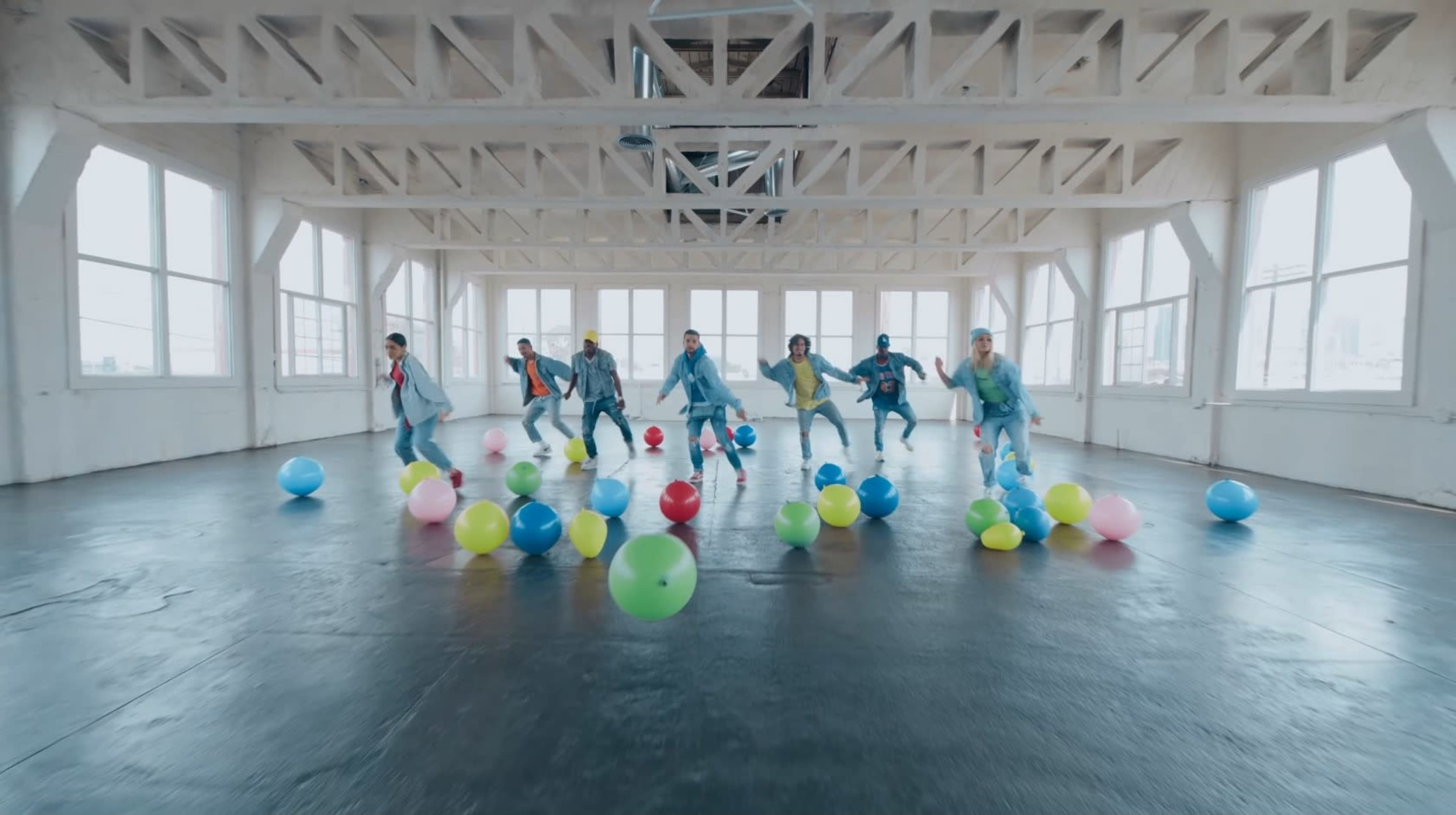 A group of dancers performs in a spacious, well-lit room filled with colorful balloons.