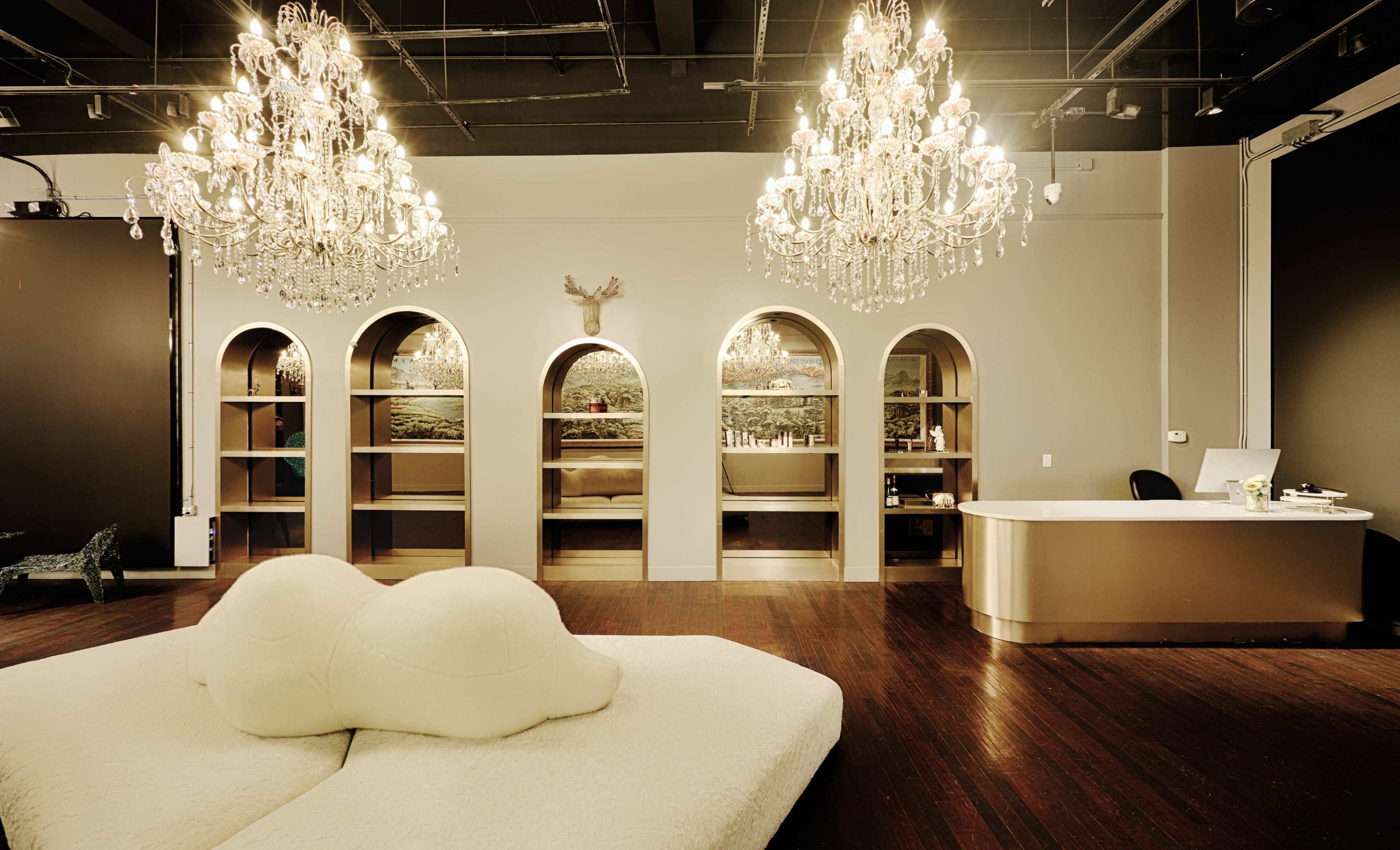 The image shows a modern reception area with two large chandeliers, a curved reception desk, and arch-shaped shelves filled with decorative items.
