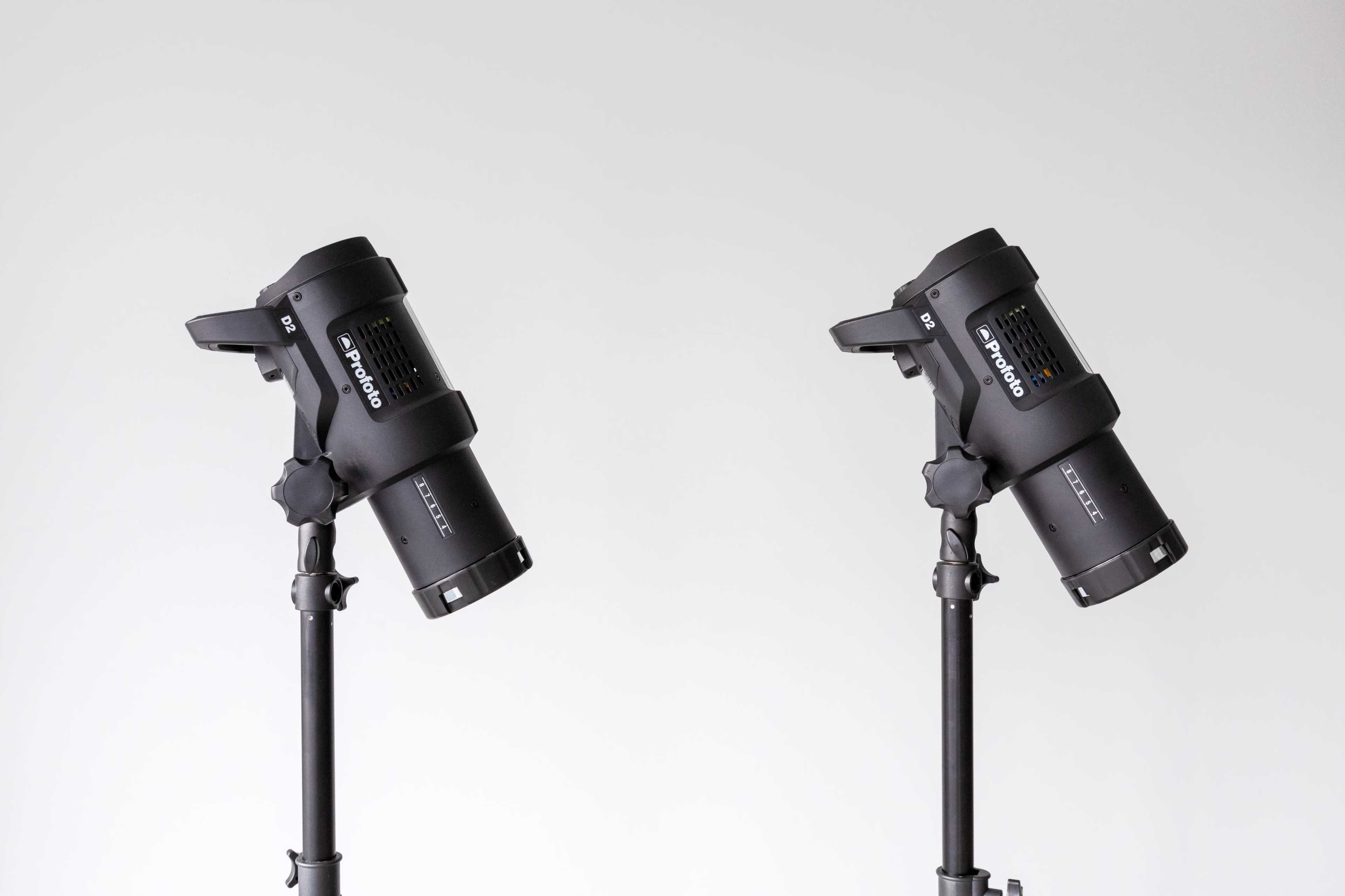 Two professional studio lights are mounted on adjustable tripods against a plain white background.