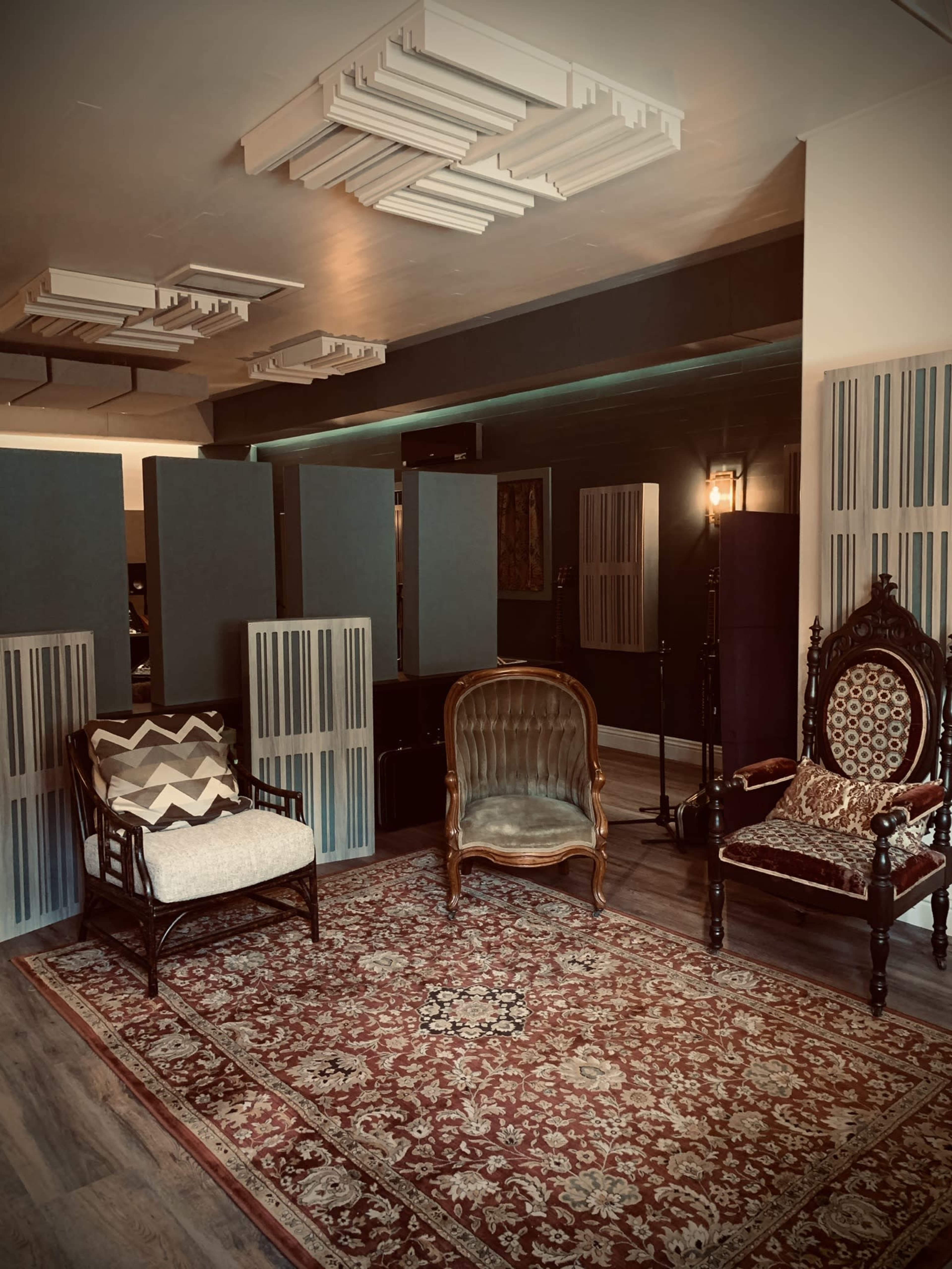 A stylish living room with two distinct chairs facing a patterned rug, separated by a series of vertical panels.