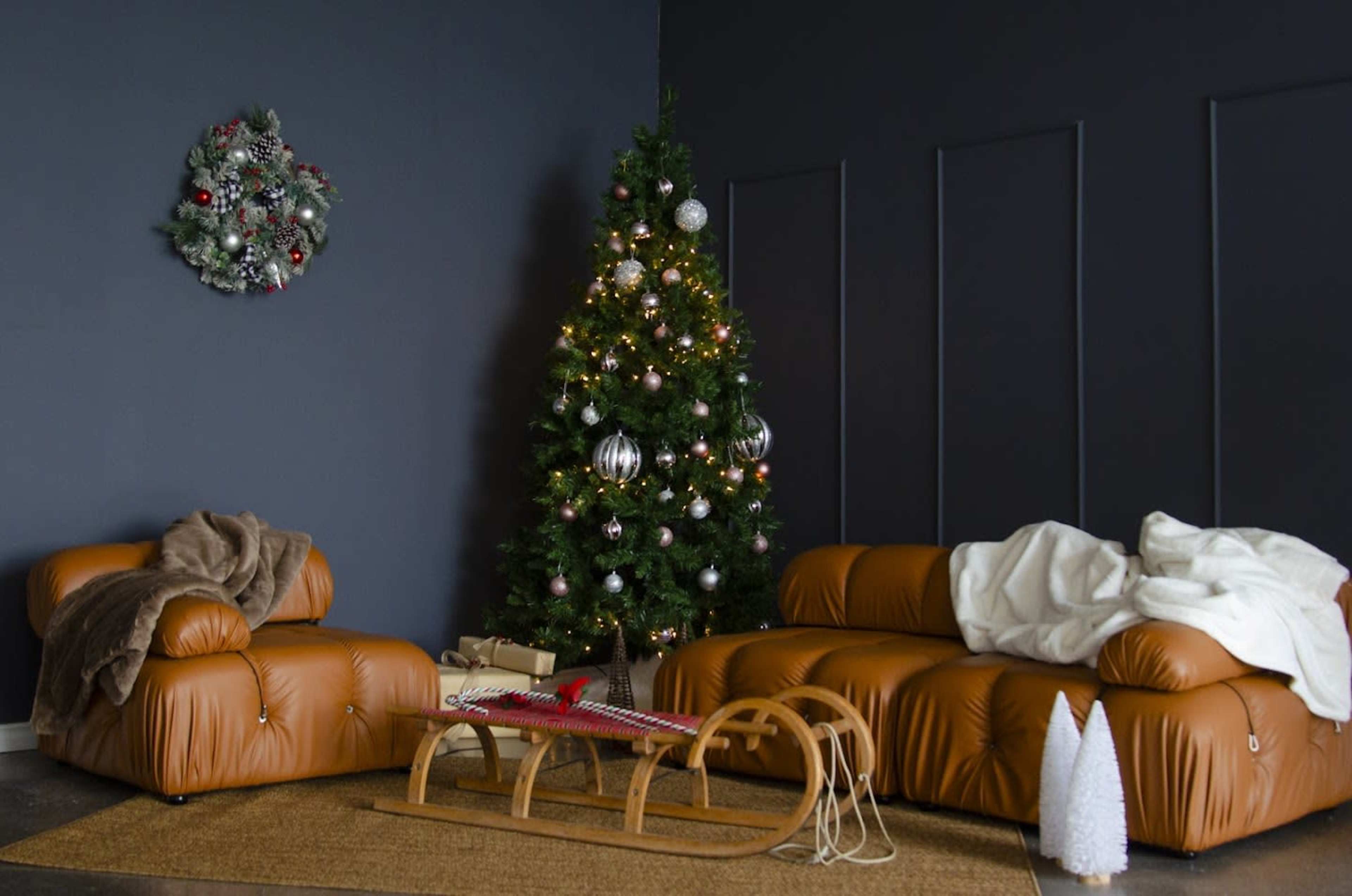 A cozy living room features a decorated Christmas tree, plush brown sofas, and a vintage sled on a jute rug.