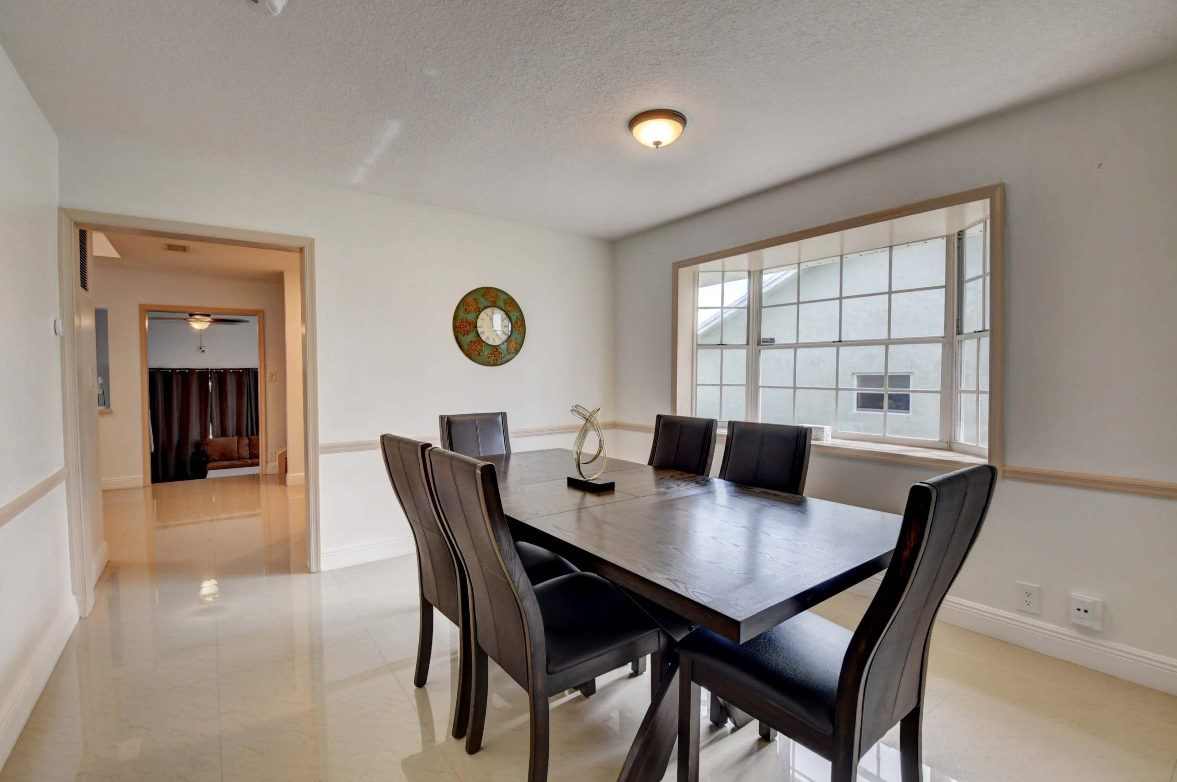 A dining area features a large wooden table surrounded by black upholstered chairs, with a window providing natural light.