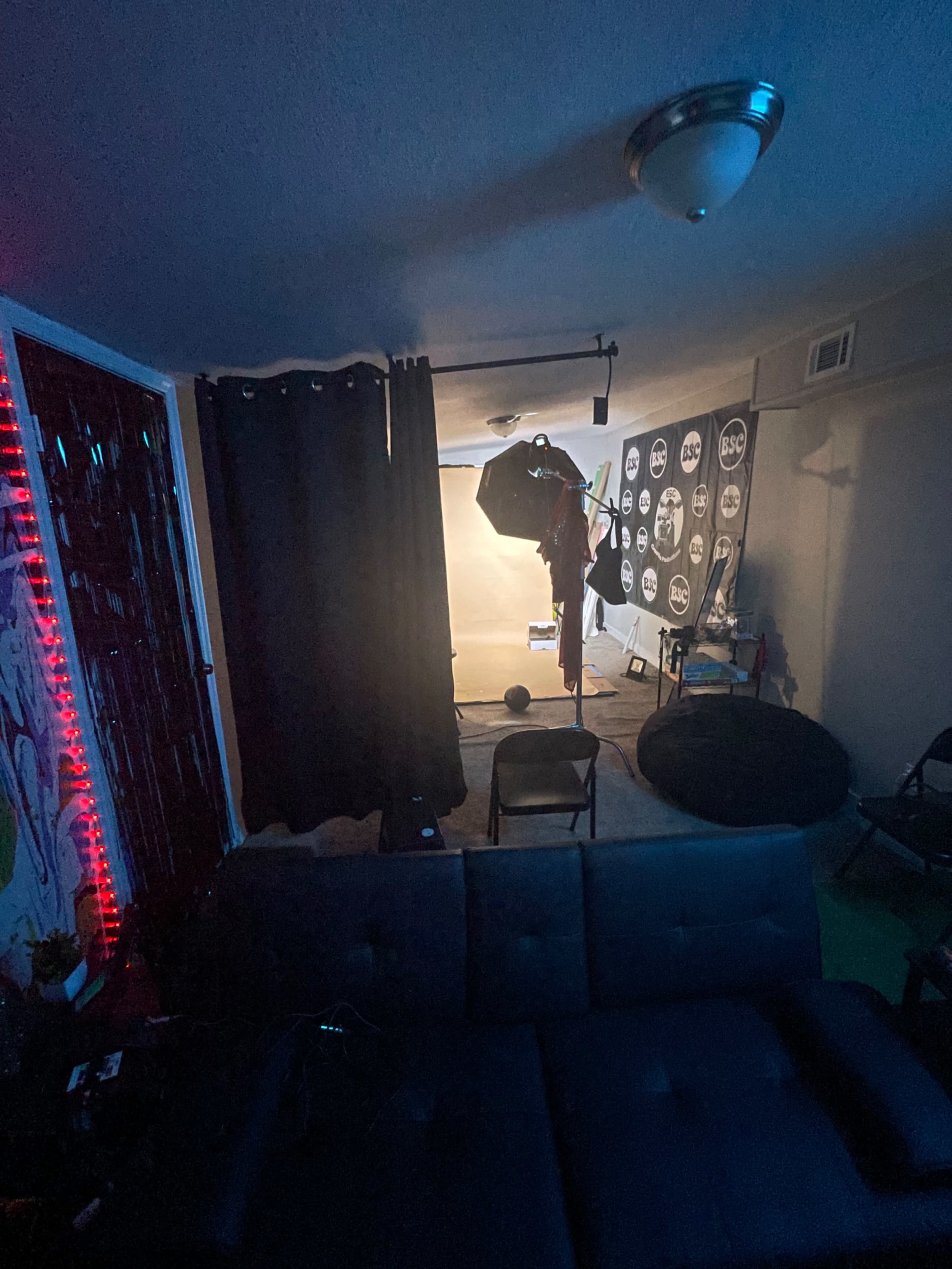 A dimly lit room features a photography setup with a backdrop, lighting equipment, and a few scattered chairs.