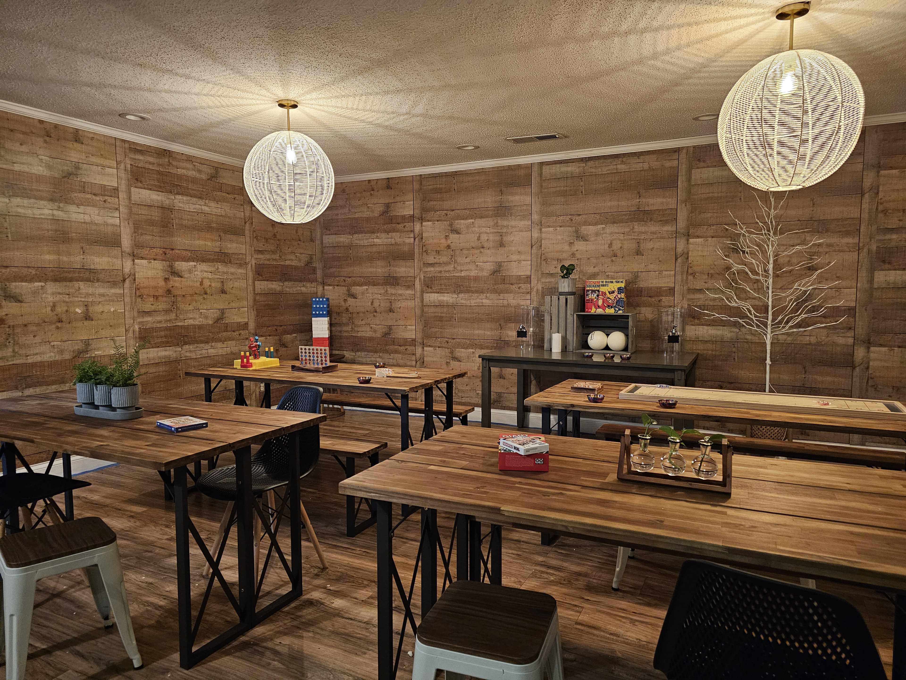 A cozy, wooden-paneled room with several wooden tables and hanging light fixtures, arranged for a group activity.