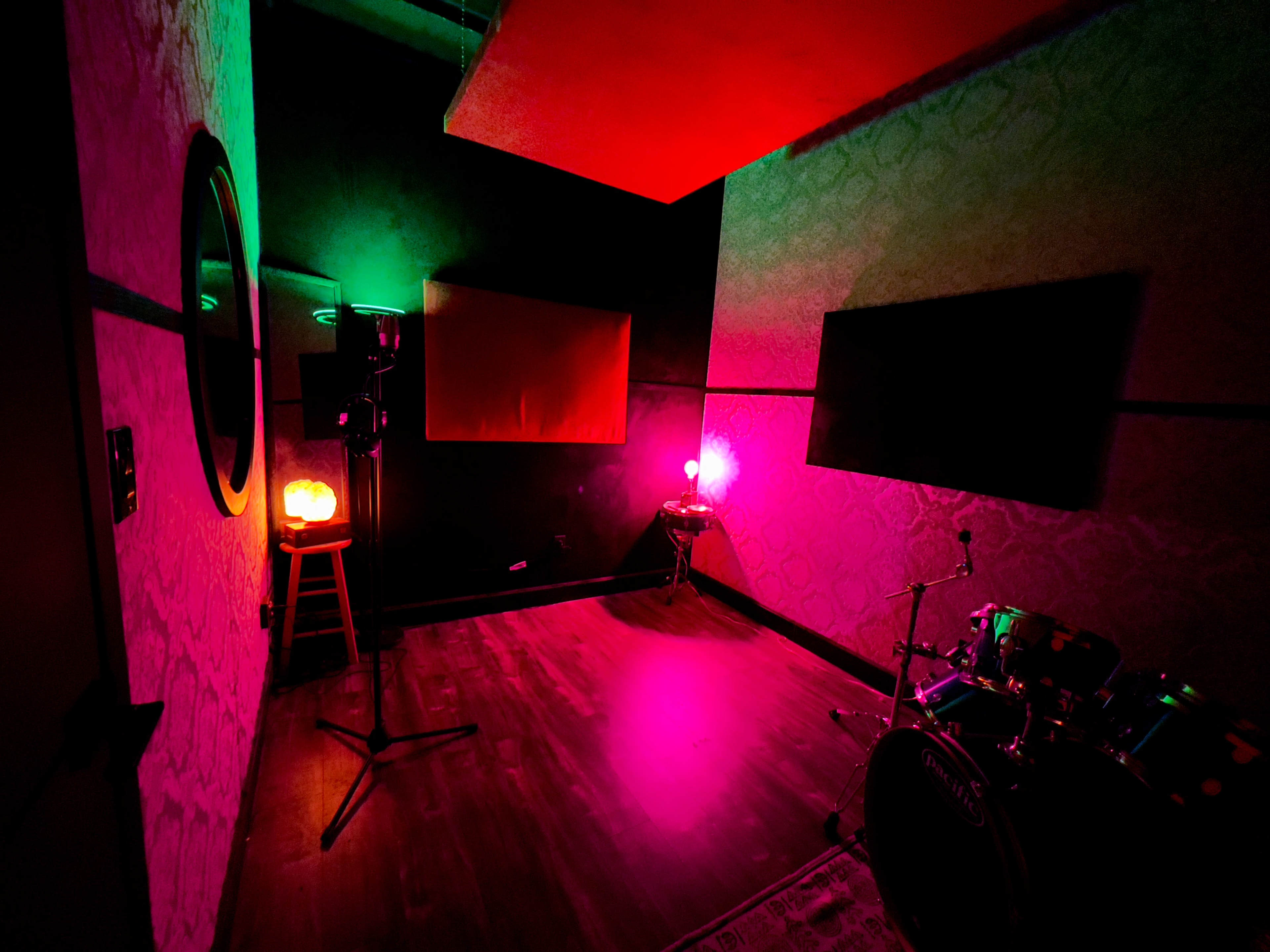 A small music studio featuring colorful lighting, a drum set, and various sound equipment.