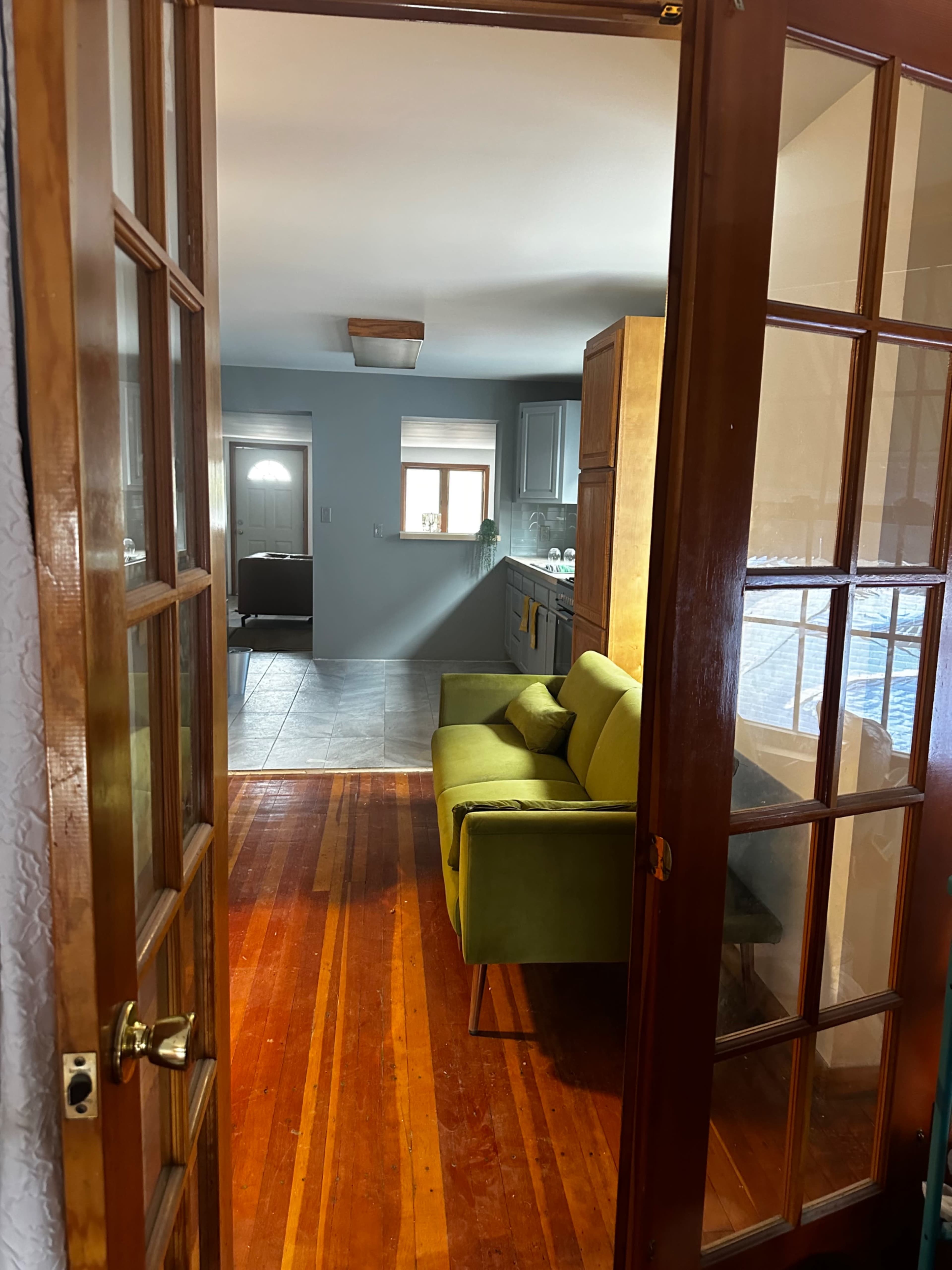 A doorway leading from a room with wooden floors to a living area featuring a green sofa and a kitchen in the background.