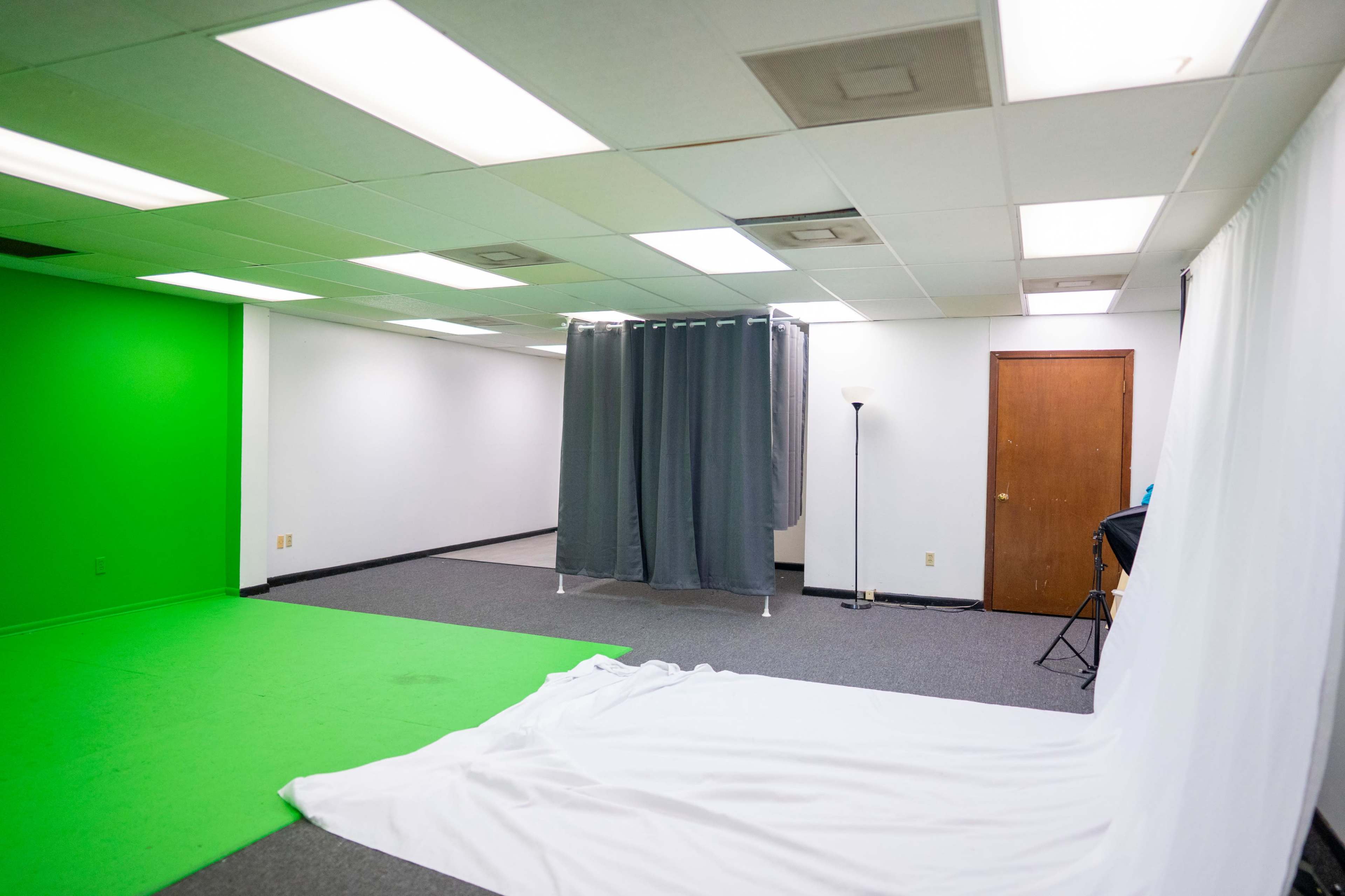 The image shows a studio space with a green screen area on one side, a white backdrop on the other, and a curtain dividing the room.