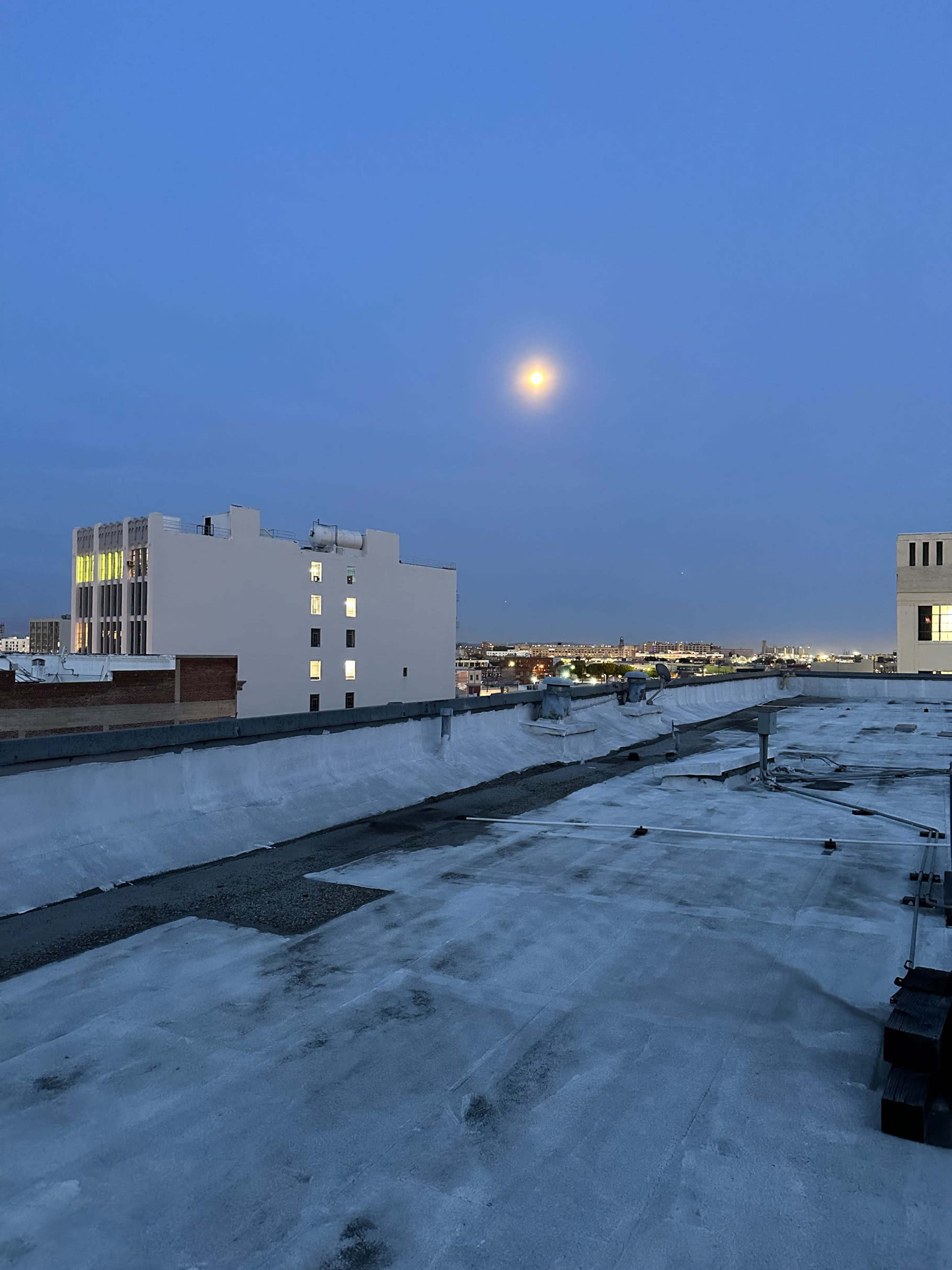 The image shows a rooftop scene at dusk, featuring a clear view of the moon and buildings in the background under a twilight sky.