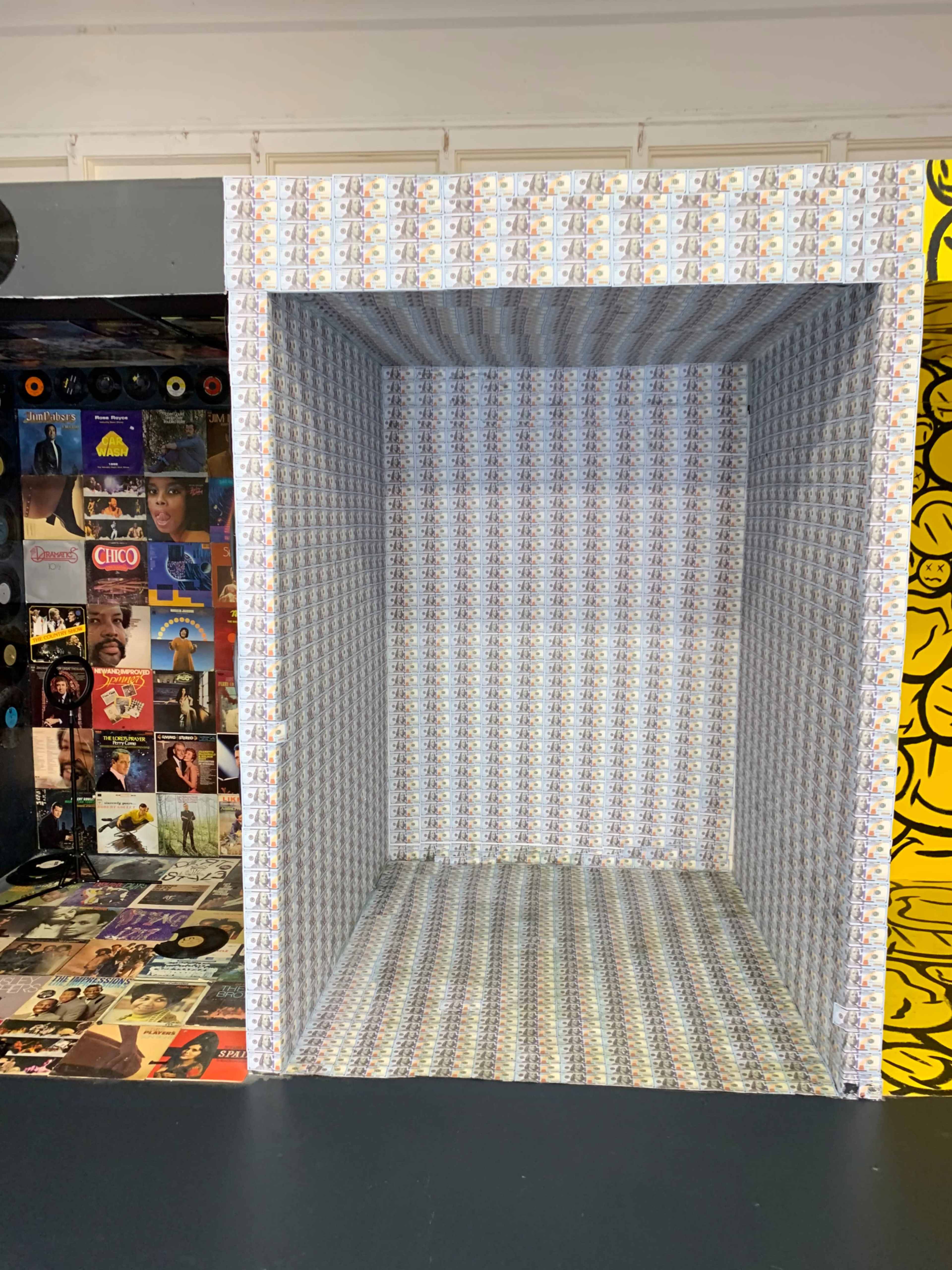 An empty, open box with patterned walls, set against a backdrop of colorful album covers.