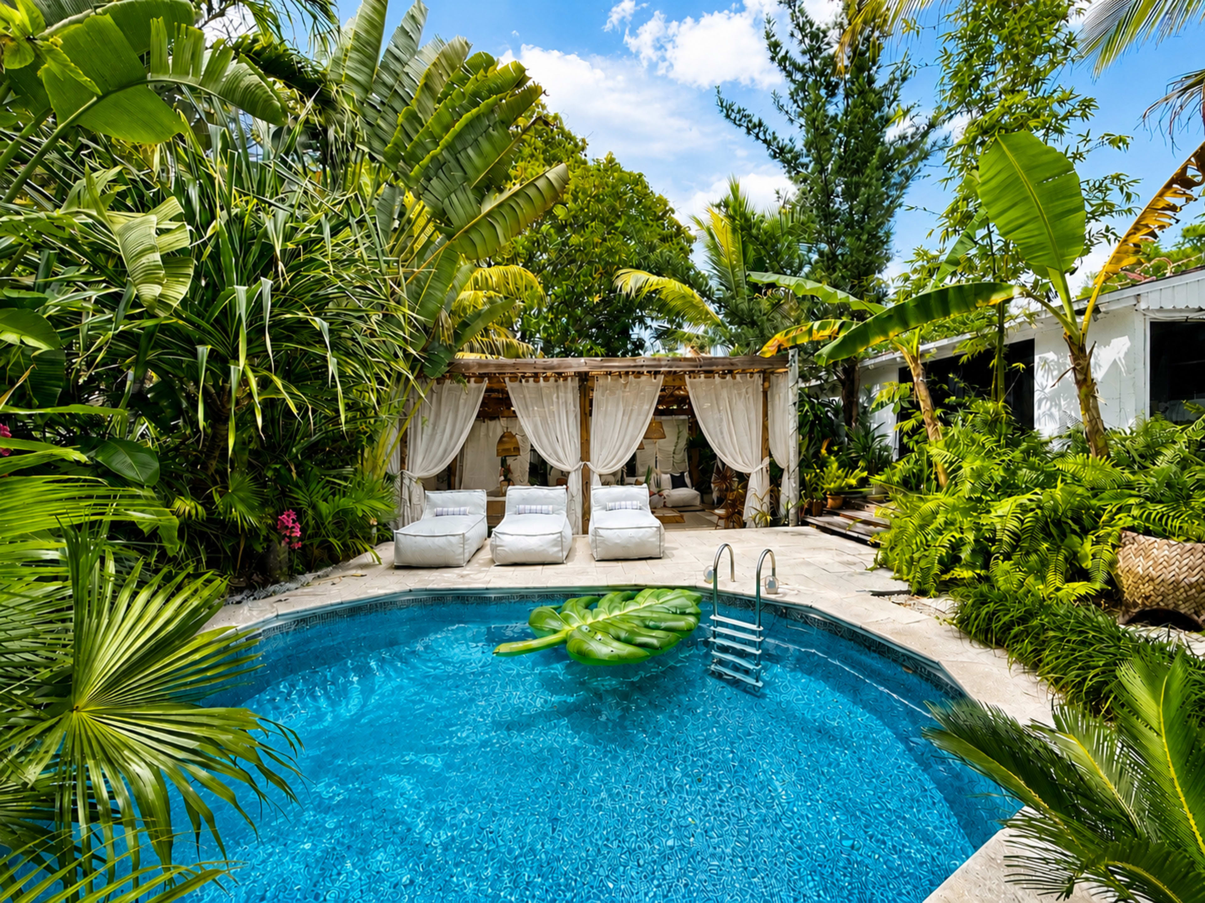 The image shows a tropical pool area surrounded by lush greenery, featuring lounge chairs and a large leaf-shaped pool float.