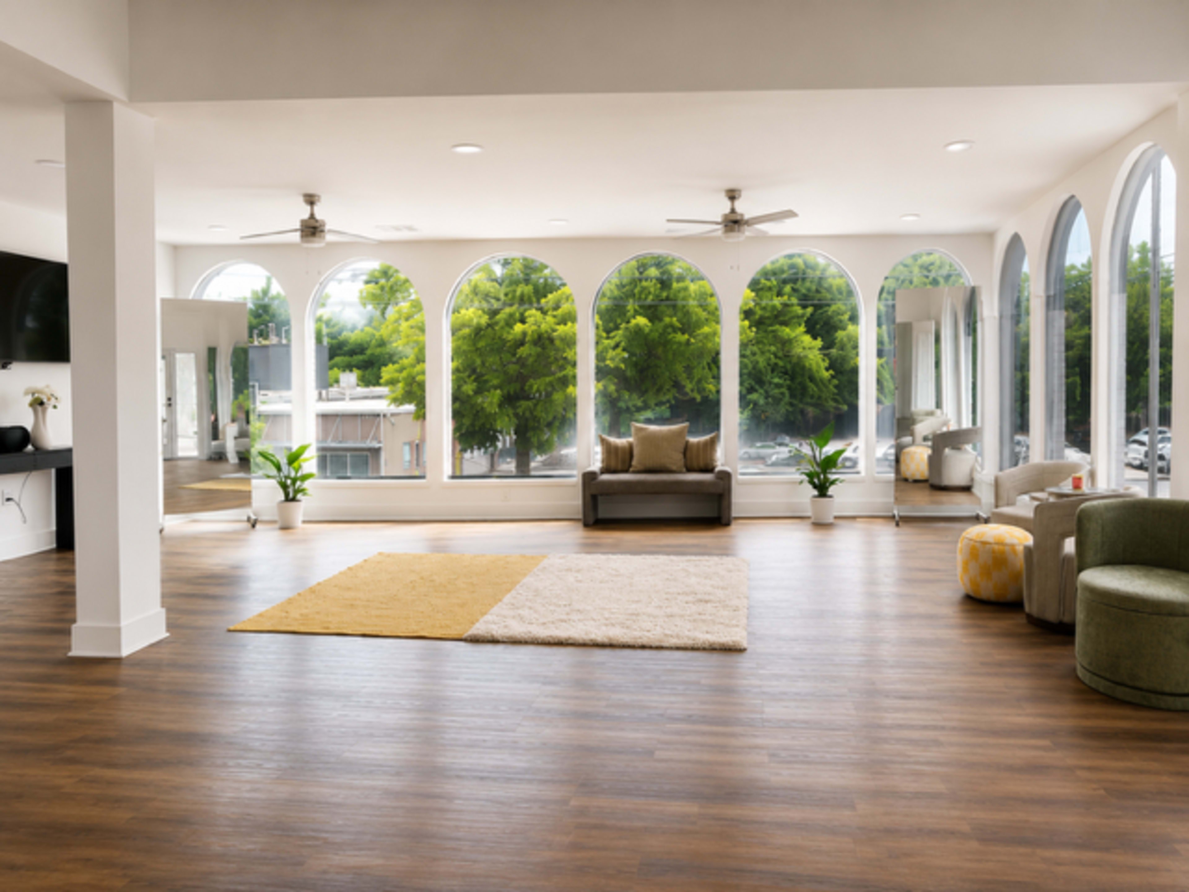 The image shows a spacious, well-lit room with large arched windows, wooden flooring, and a few pieces of furniture, including a sofa and chairs.