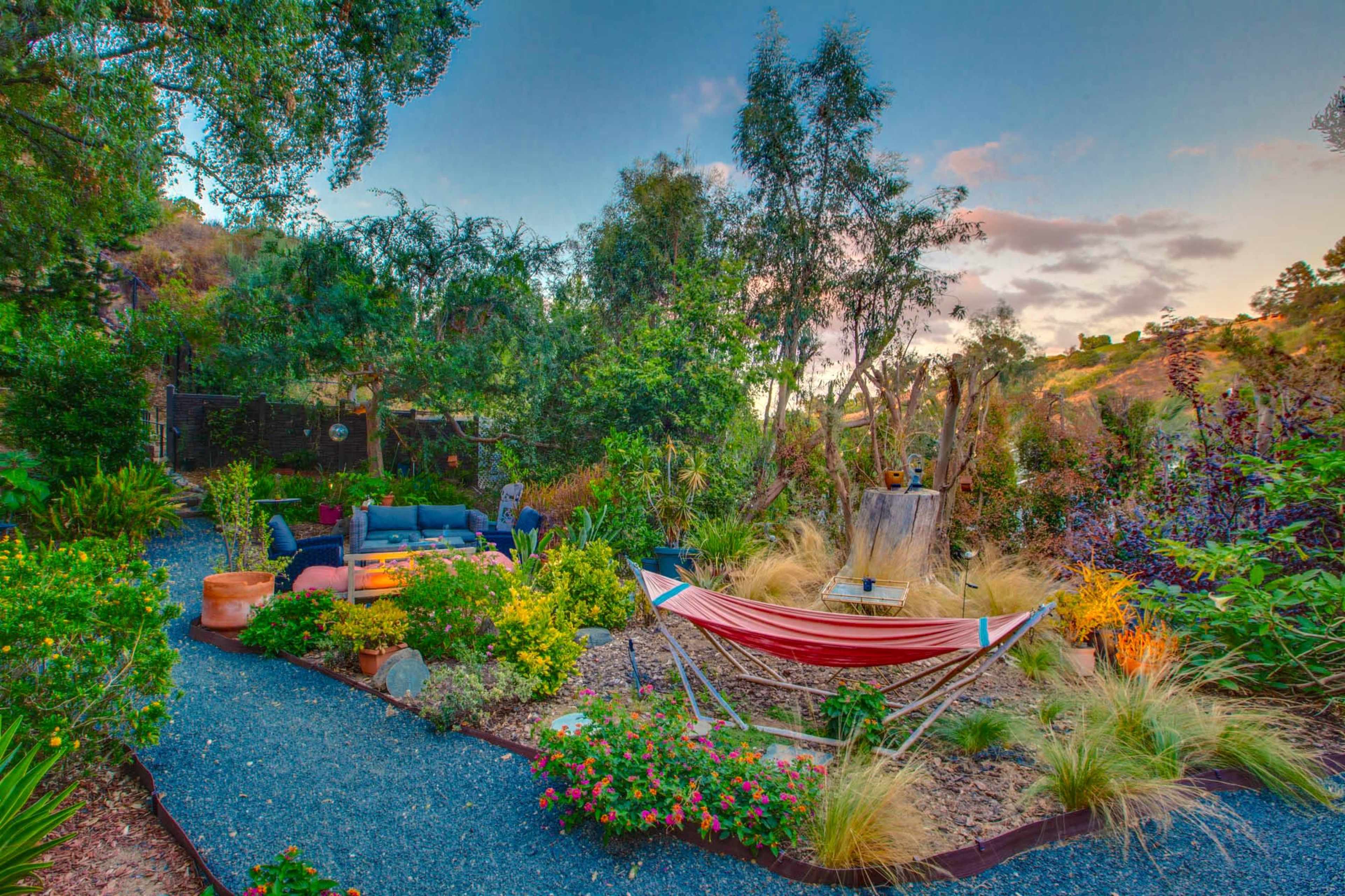 The image features a lush garden with a hammock, seating area, and various plants along a gravel path.