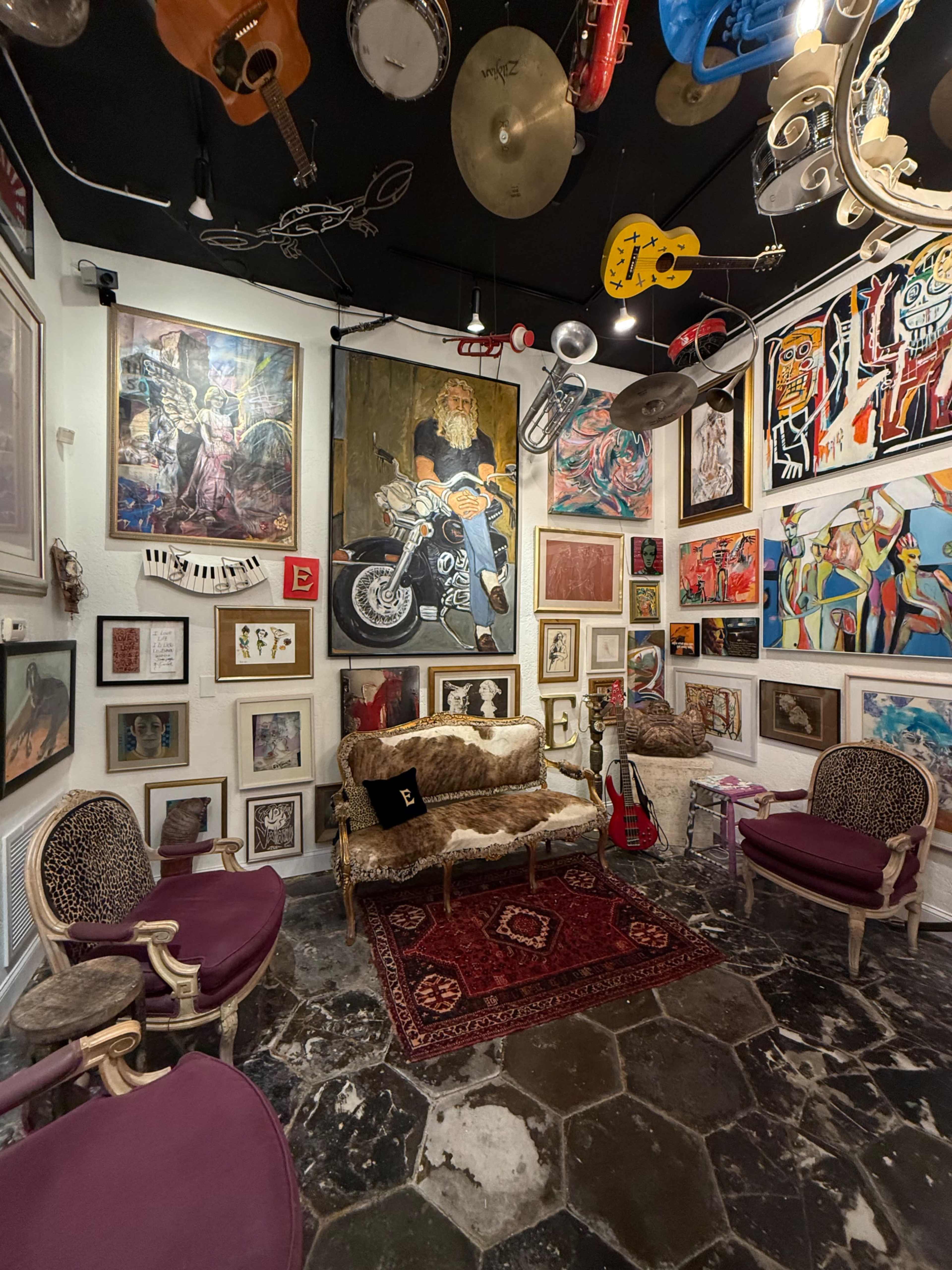 The scene features a creatively decorated room with various artworks on the walls, a vintage sofa, and several musical instruments hanging from the ceiling.
