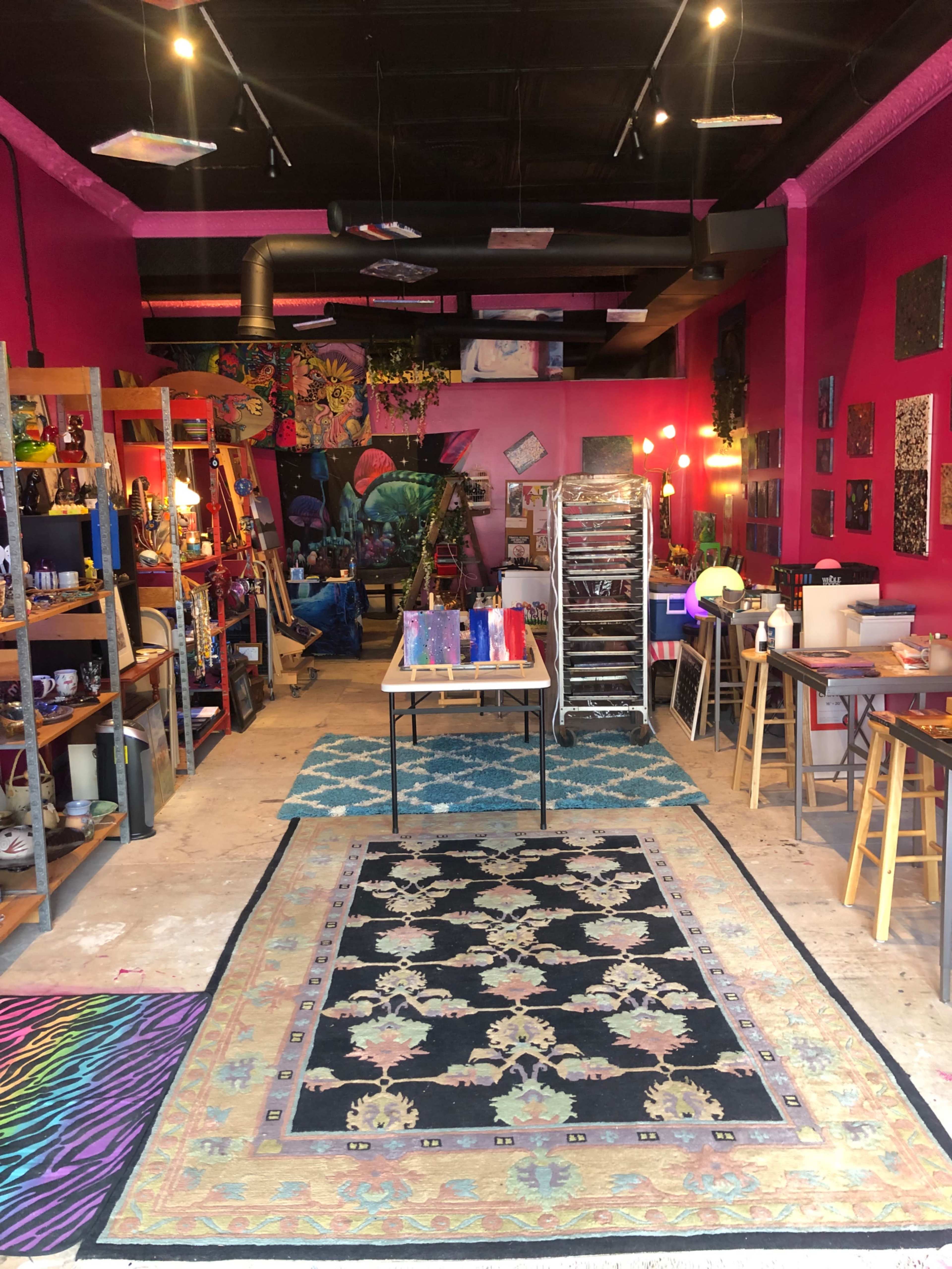 A vibrant art studio with pink walls, various art supplies on shelves, and two patterned rugs on the floor.