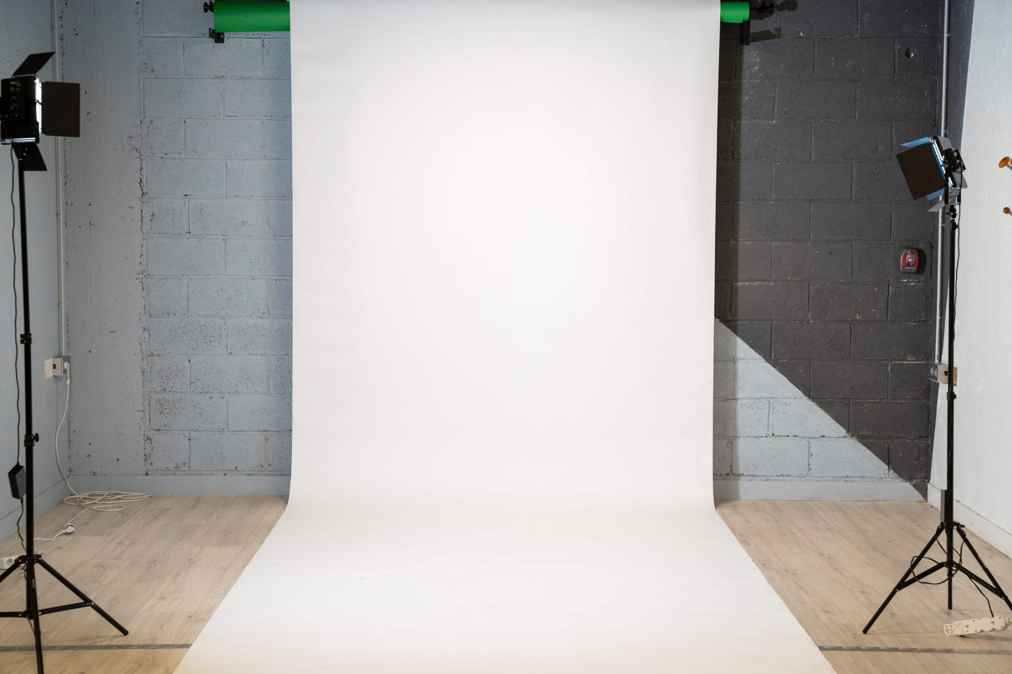 A photography studio features a white backdrop and two lighting setups on either side.