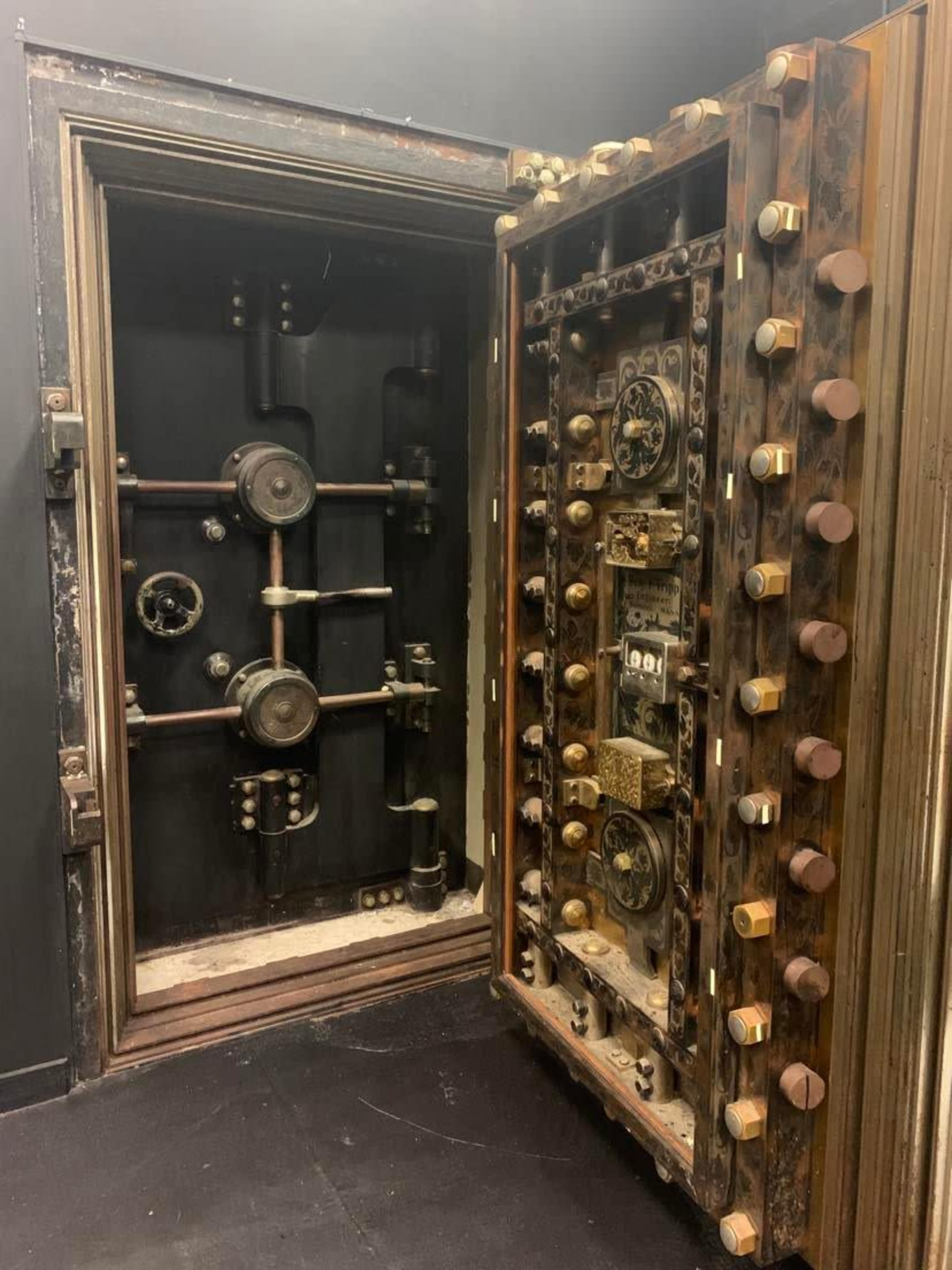 The image shows an ornate, vintage safe with intricate dials and mechanisms, partially open to reveal its inner workings.