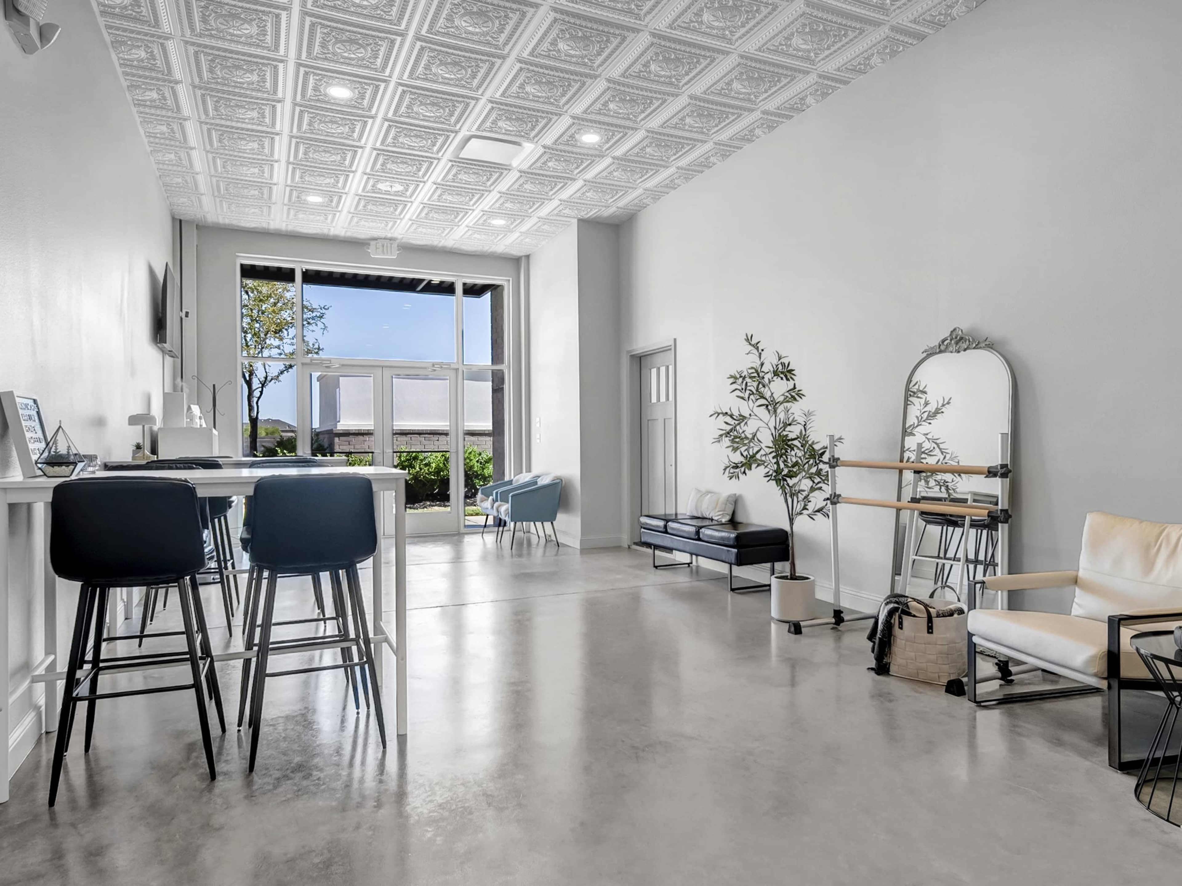 The image shows a modern, open interior space with a decorative ceiling, featuring seating areas and a large window that allows natural light to enter.