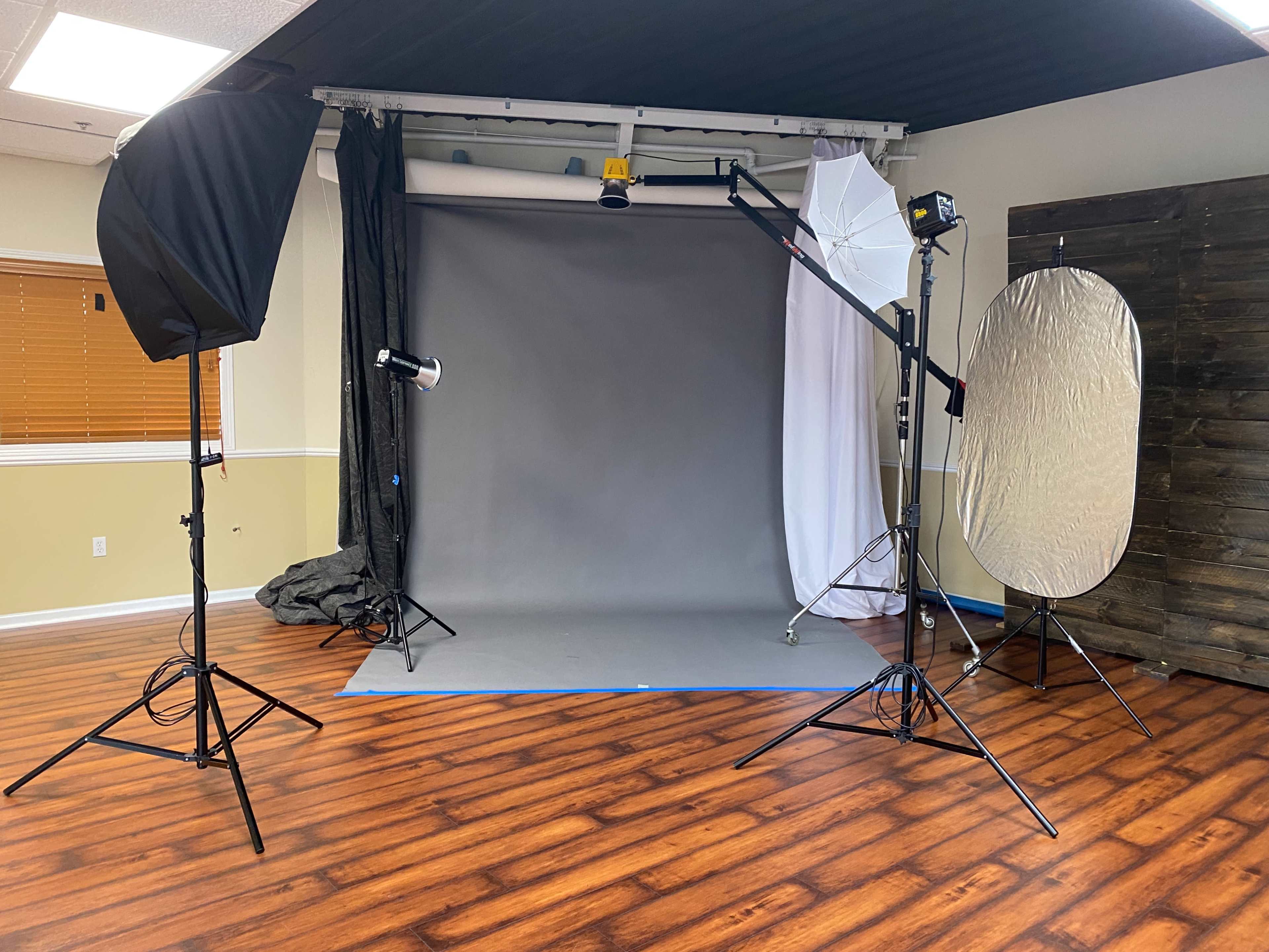 A photography studio setup with a gray backdrop, various lighting equipment, and a reflector.