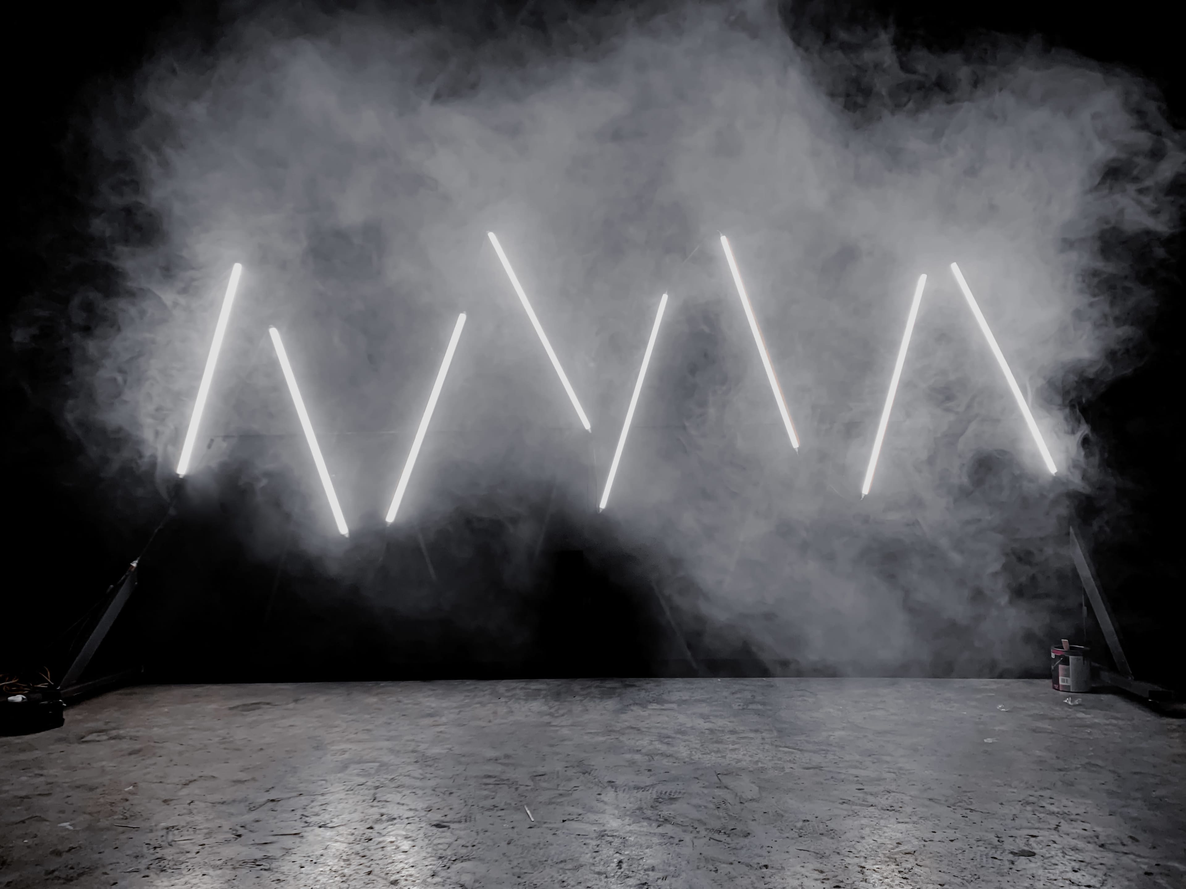 Angled neon lights arranged in a zigzag pattern against a backdrop of smoke.