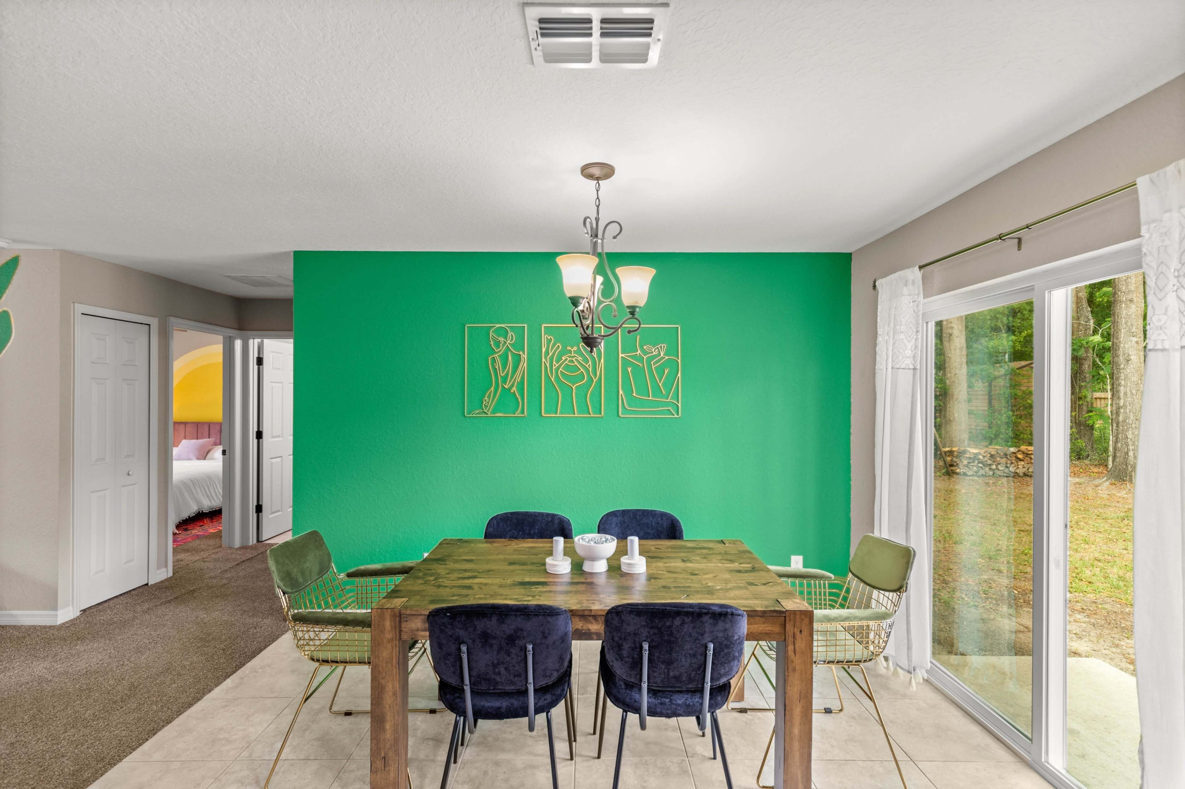 A dining area features a green accent wall, a wooden table surrounded by chairs, and a sliding glass door leading to an outdoor space.