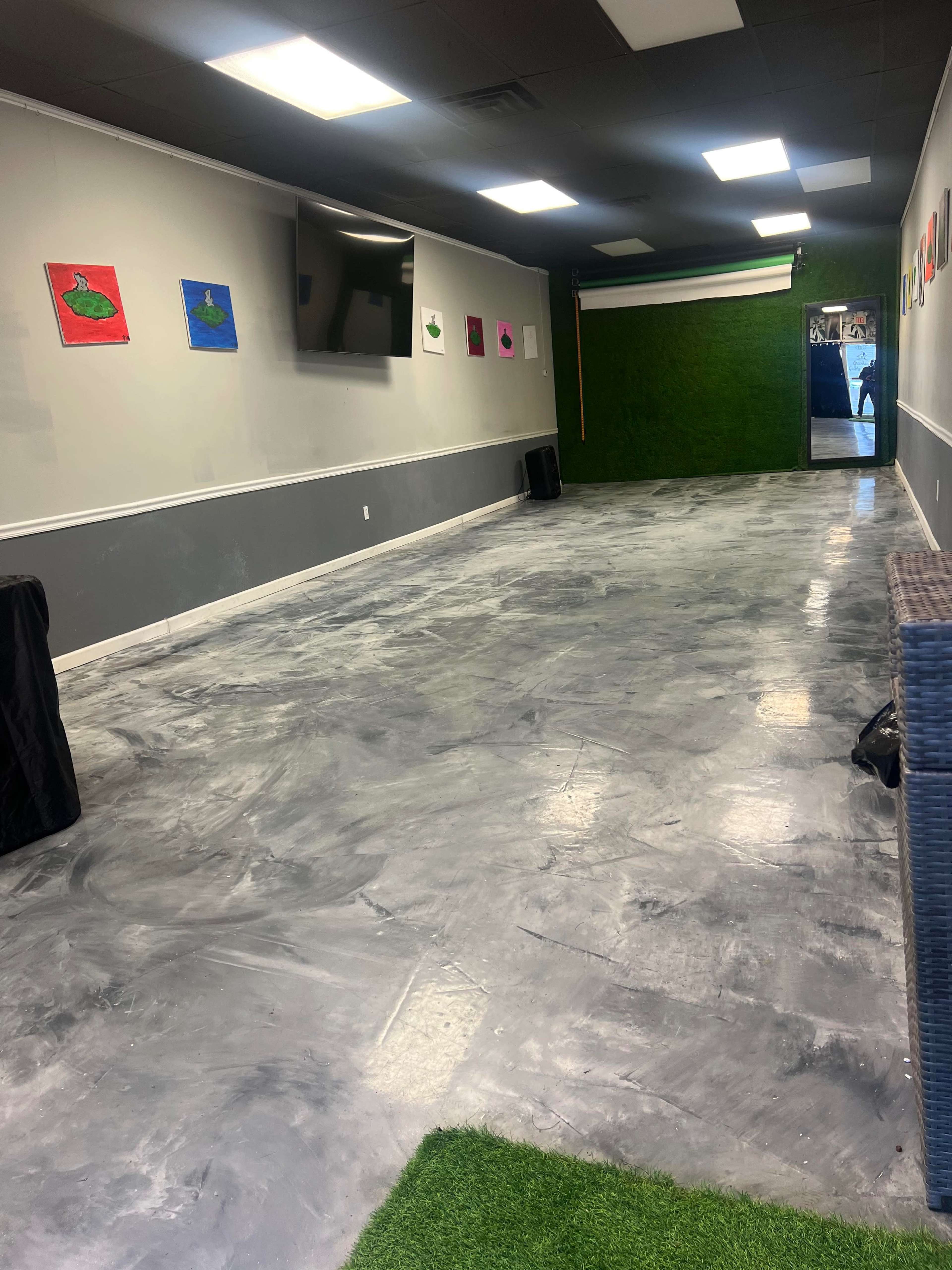 An empty room with a polished gray floor, green grass-like turf in one corner, and colorful artwork on the walls.