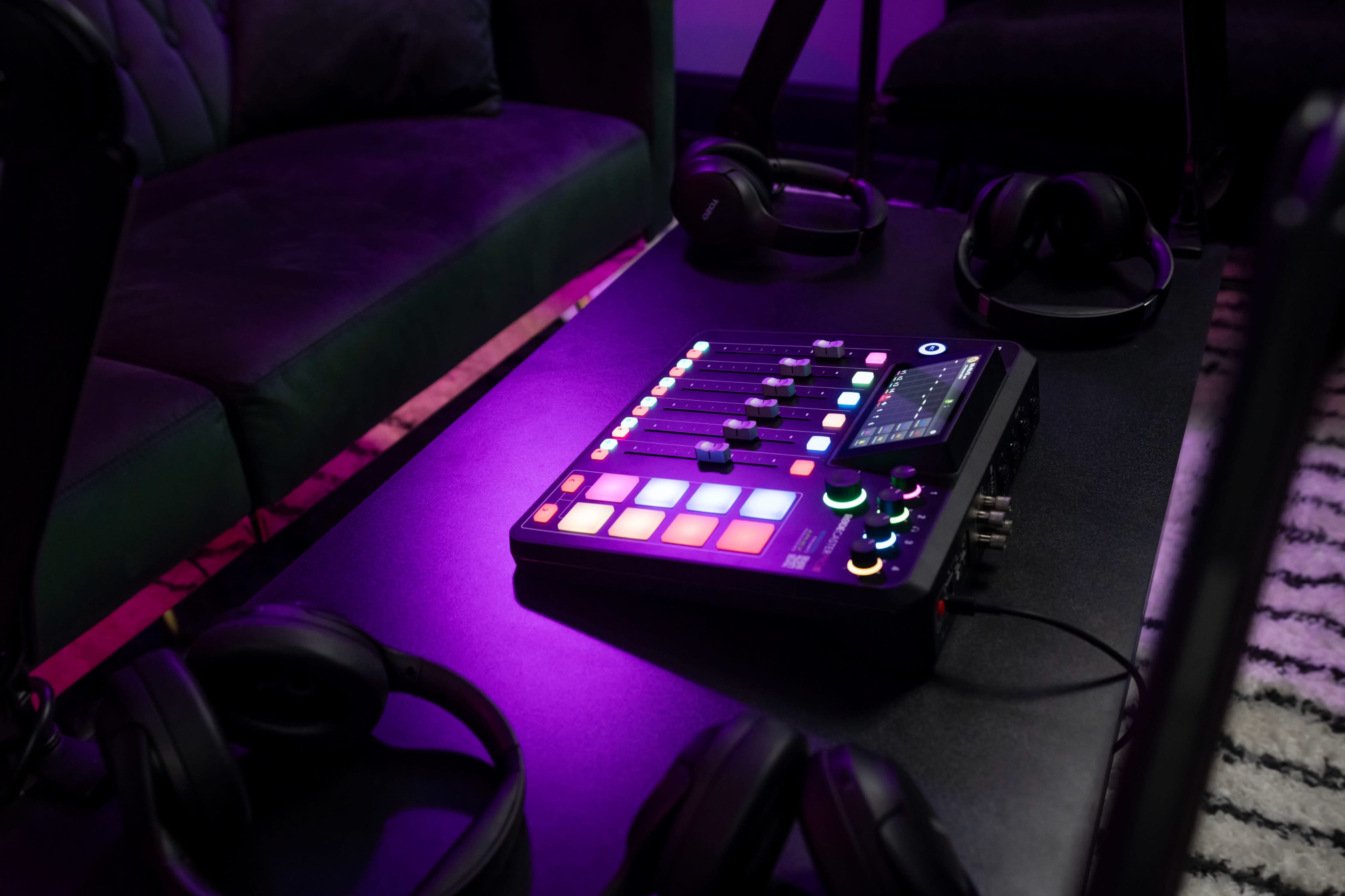 A music production controller and several pairs of headphones rest on a black table beside a green couch in a dimly lit room.