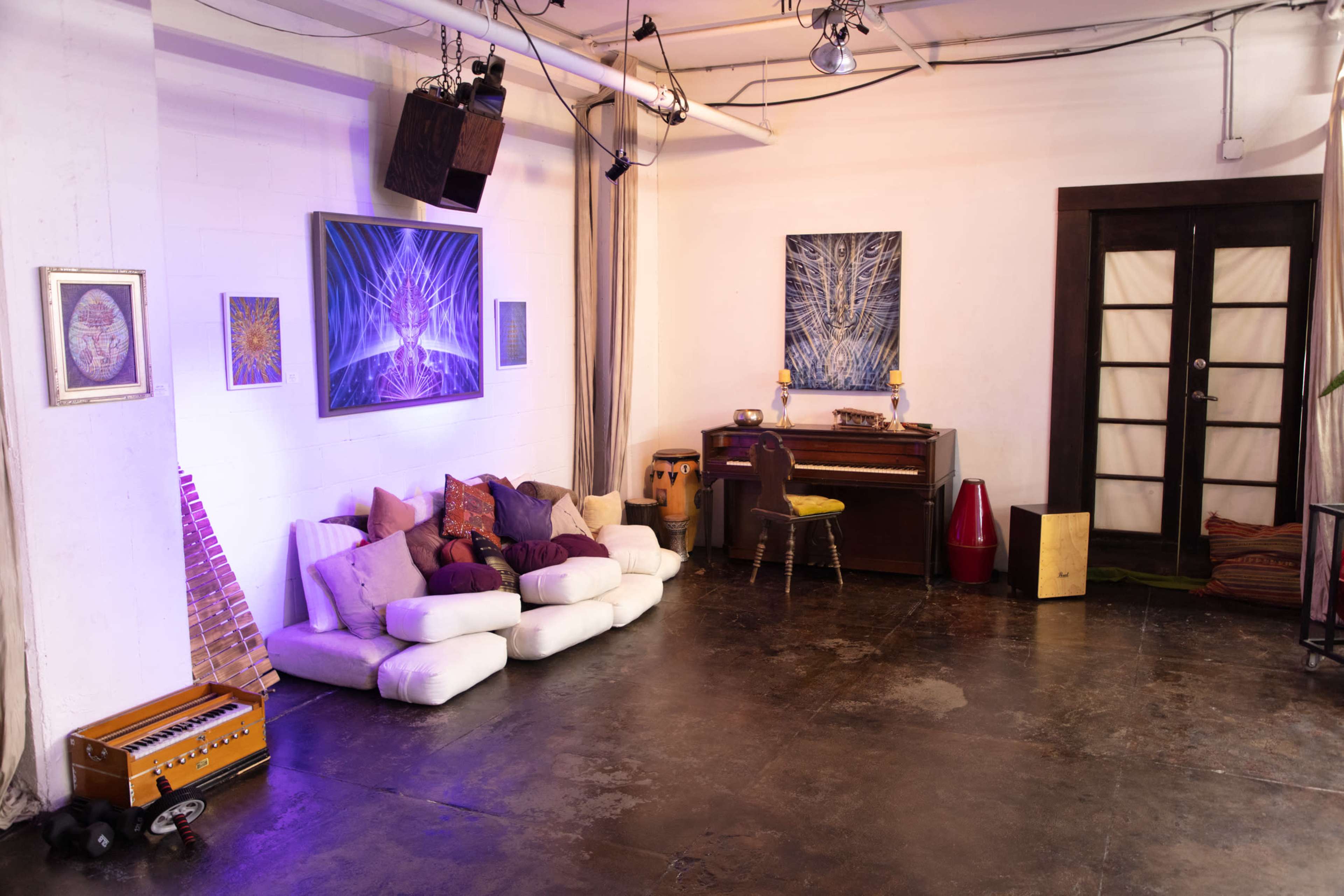 A spacious studio with a seating area on the left, a piano in the center, and various artworks hanging on the walls.