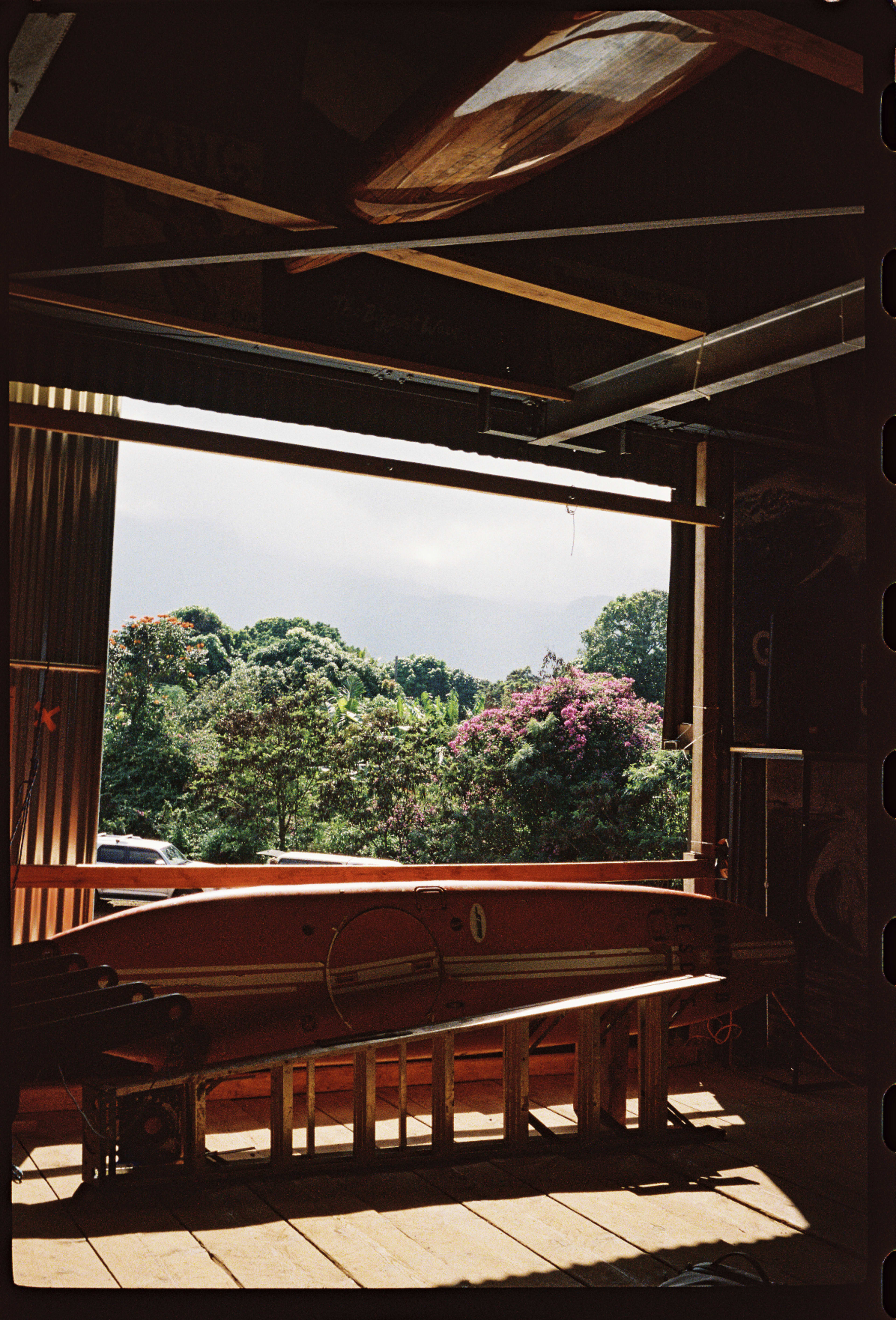 A view of a workshop with an orange kayak resting on a wooden table, framed by an open doorway showcasing vibrant greenery outside.