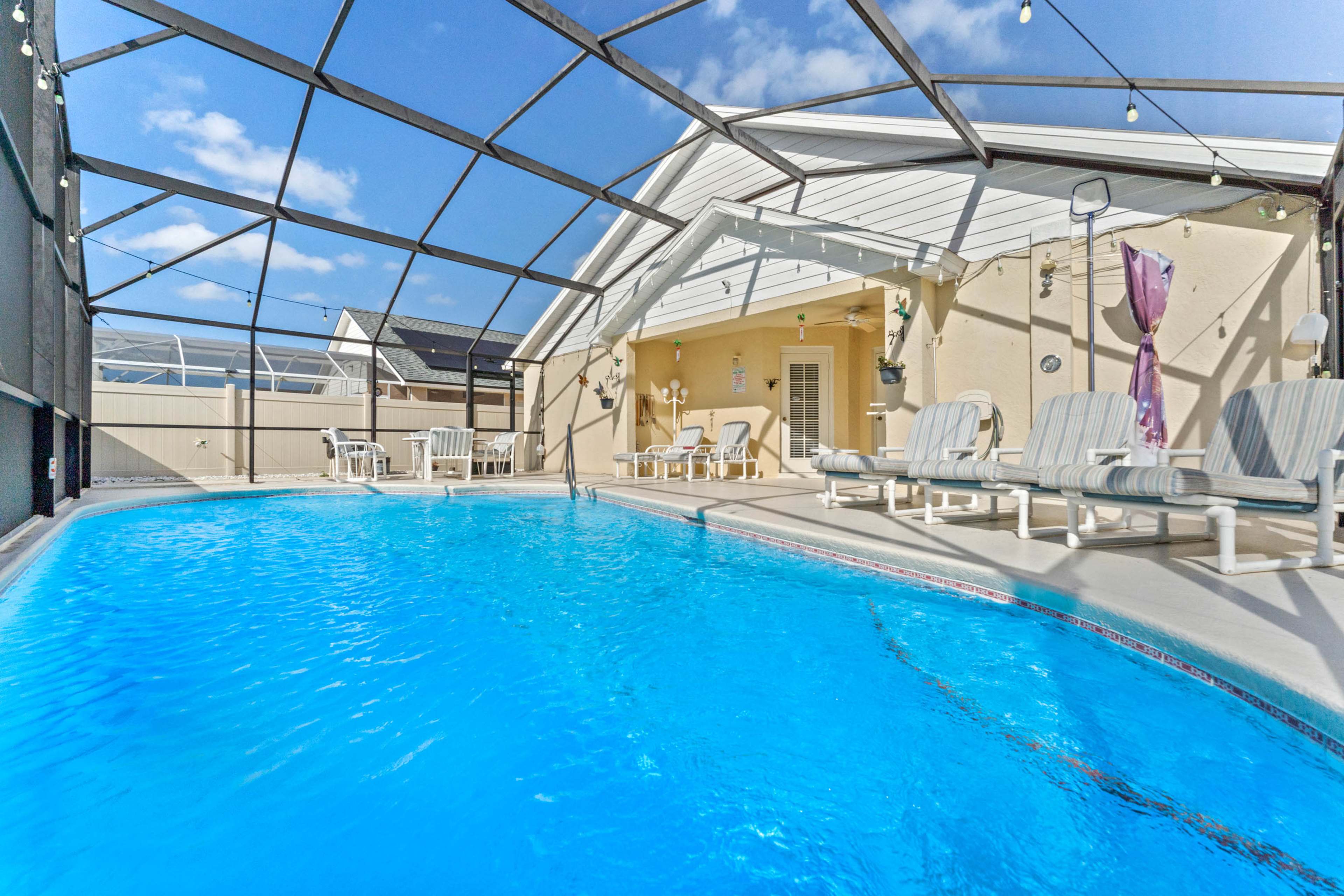 The image shows an outdoor swimming pool surrounded by a screened enclosure, with lounge chairs set up nearby.