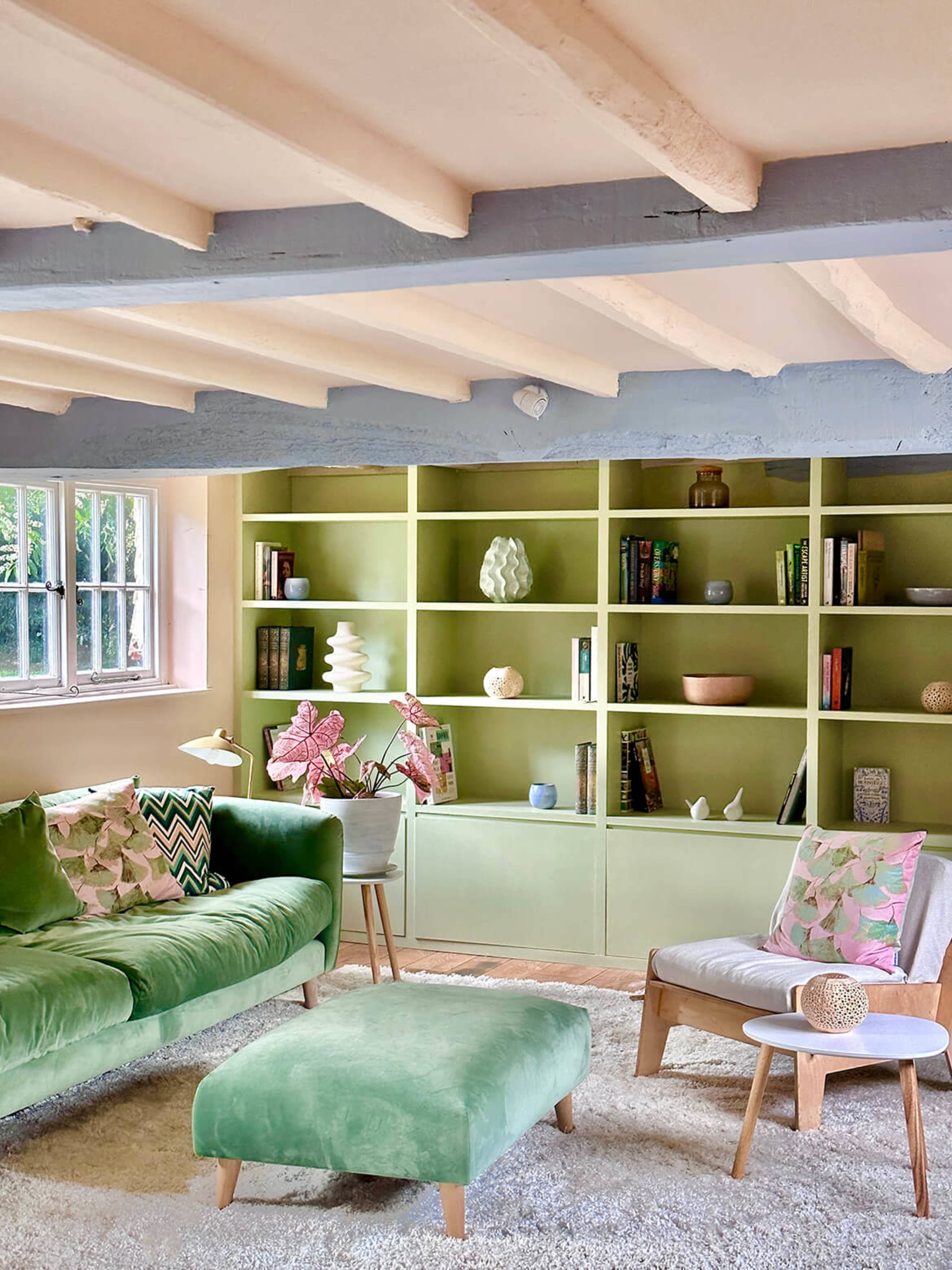 The image depicts a living room with a light green bookshelf, a green sofa, and a coffee table, accompanied by decorative pillows and a textured rug.