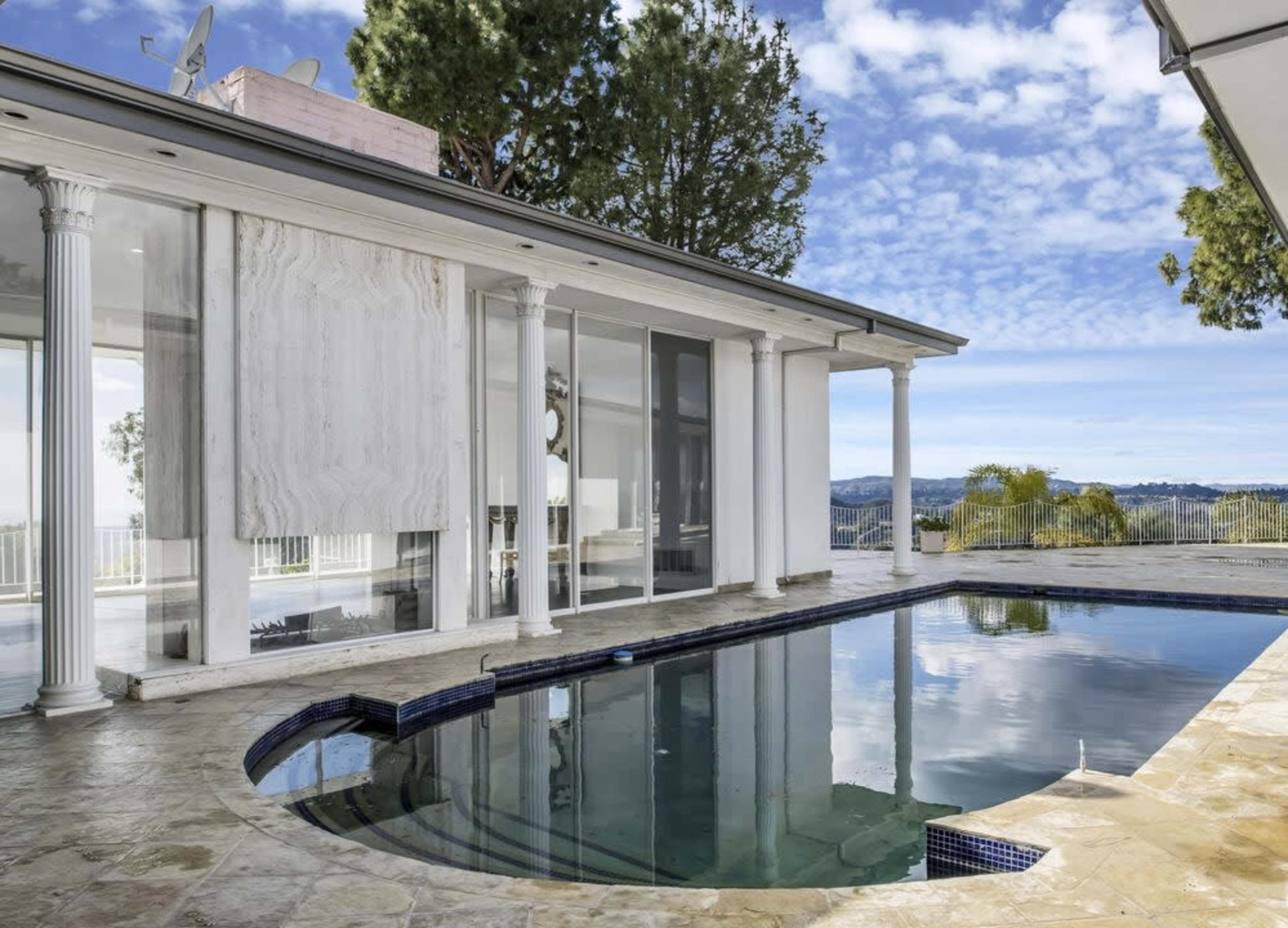 The image features a modern home with a pool, large glass windows, and columns overlooking a scenic landscape.