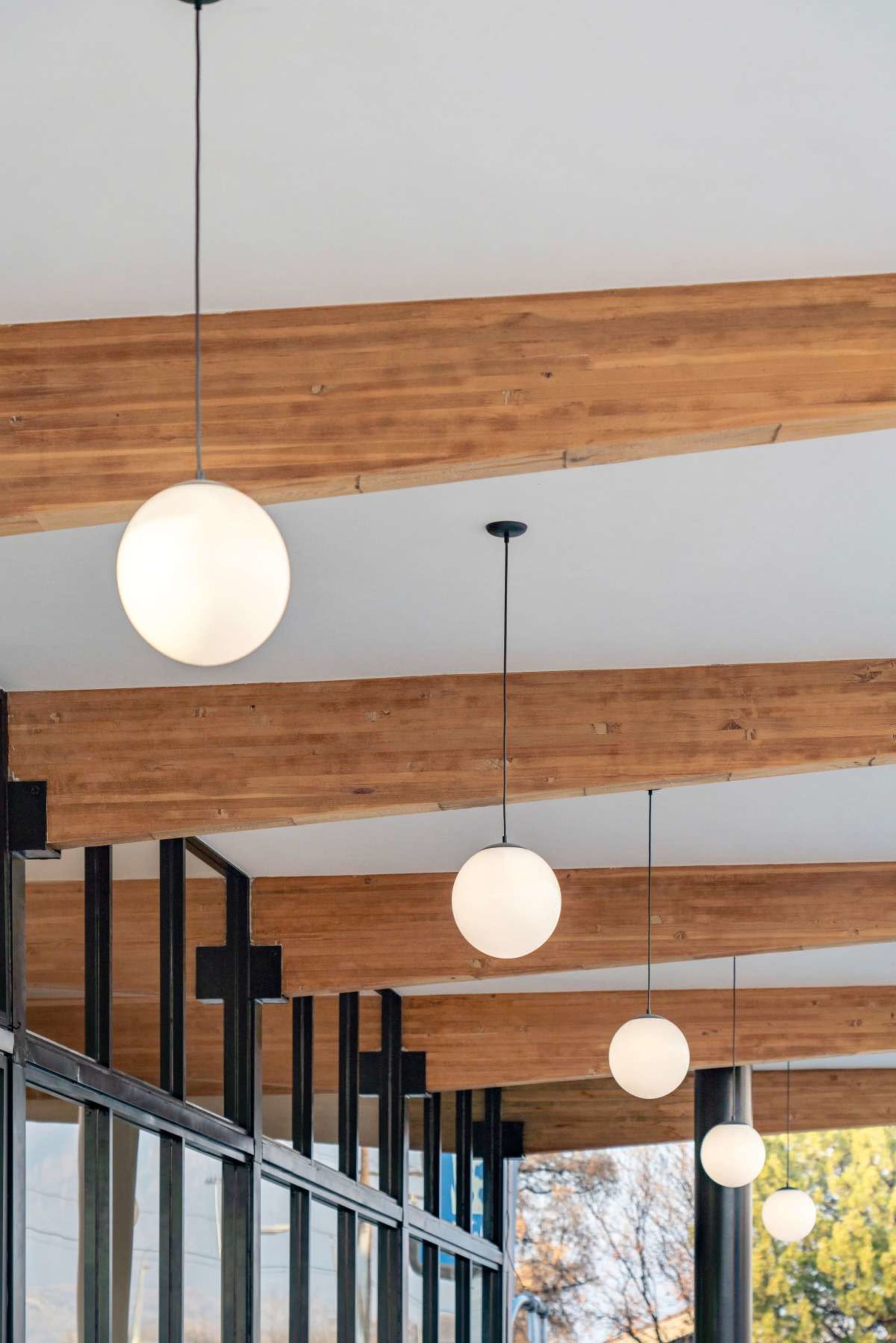 The image shows a row of round pendant lights hanging from a wooden-beam ceiling over a glass storefront.