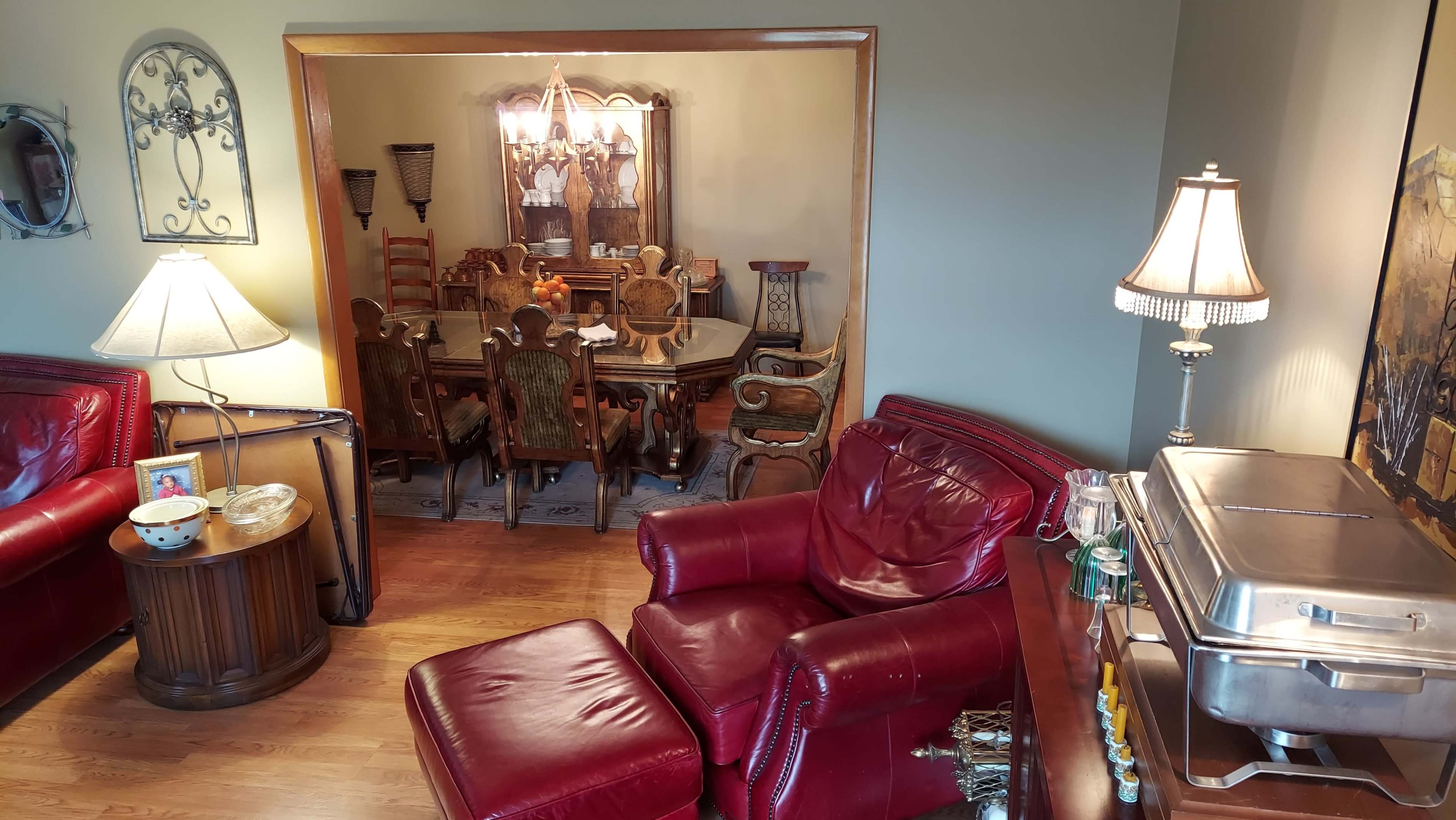 A living room with red leather chairs and a wooden table, leading to a dining area with a large table surrounded by ornate chairs.