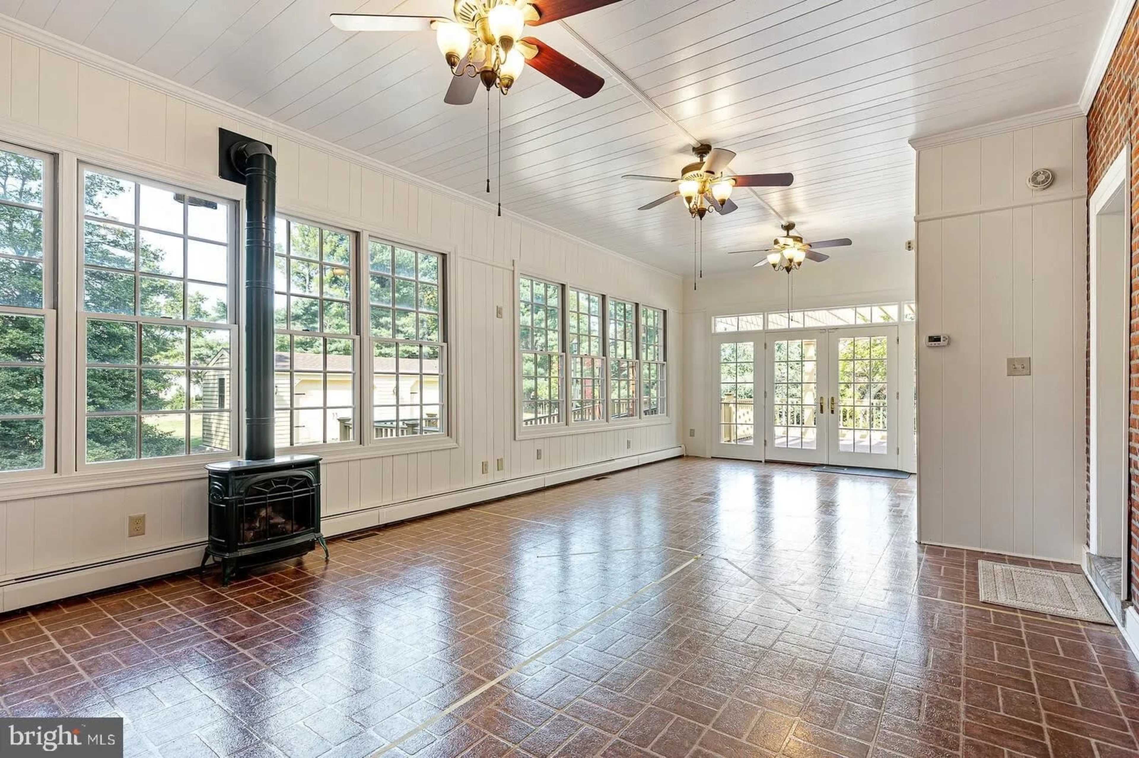 A spacious sunroom with multiple windows, a wooden ceiling, and a stove in one corner.