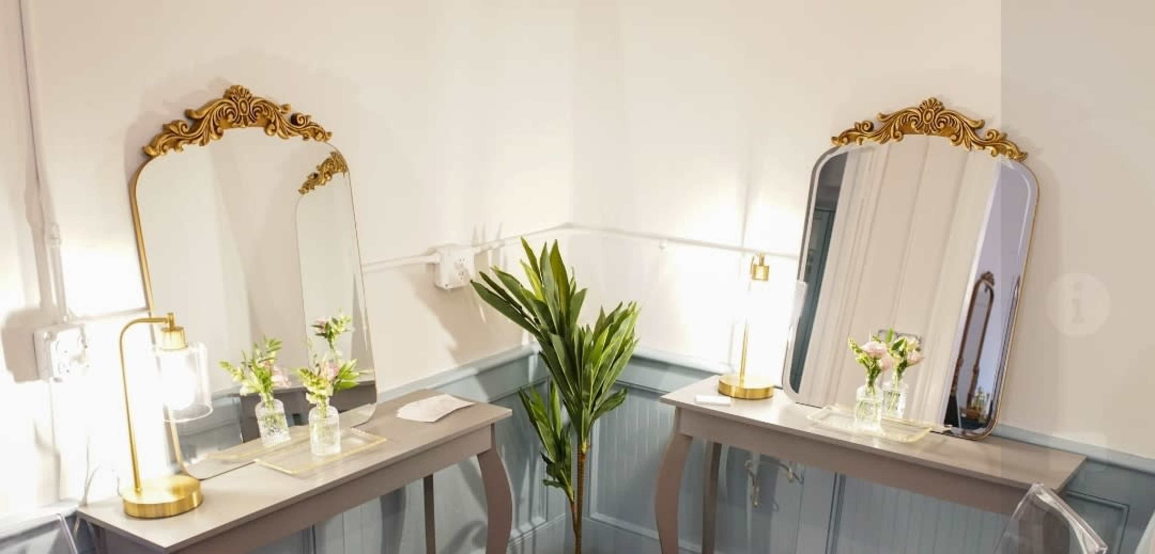 Two elegantly designed vanity tables with mirrors, lamps, and small vases of flowers in a well-lit room.