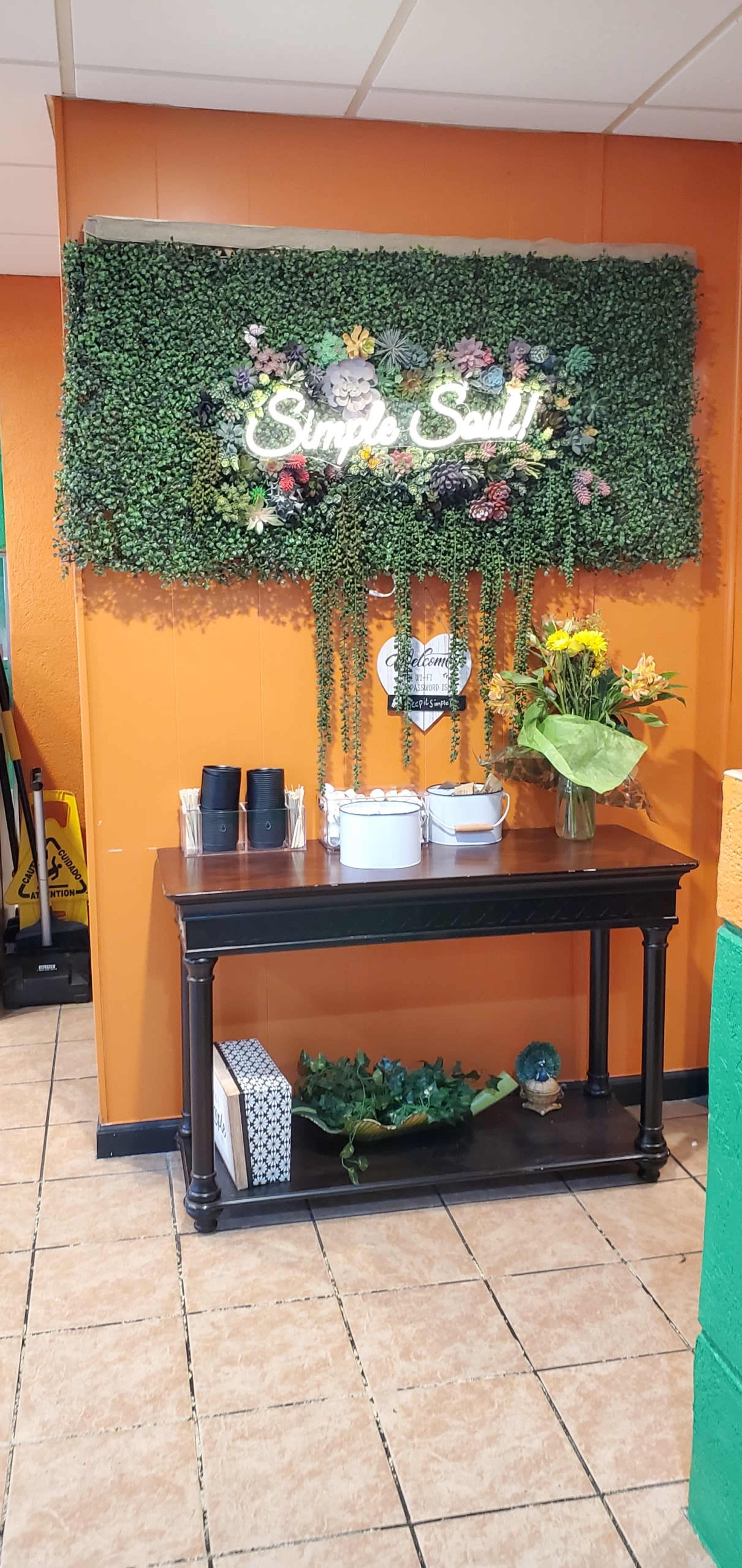 A small indoor entryway with a green decorative wall, a wooden table displaying a white container and sunflowers, and a sign that reads "Simple Soul."