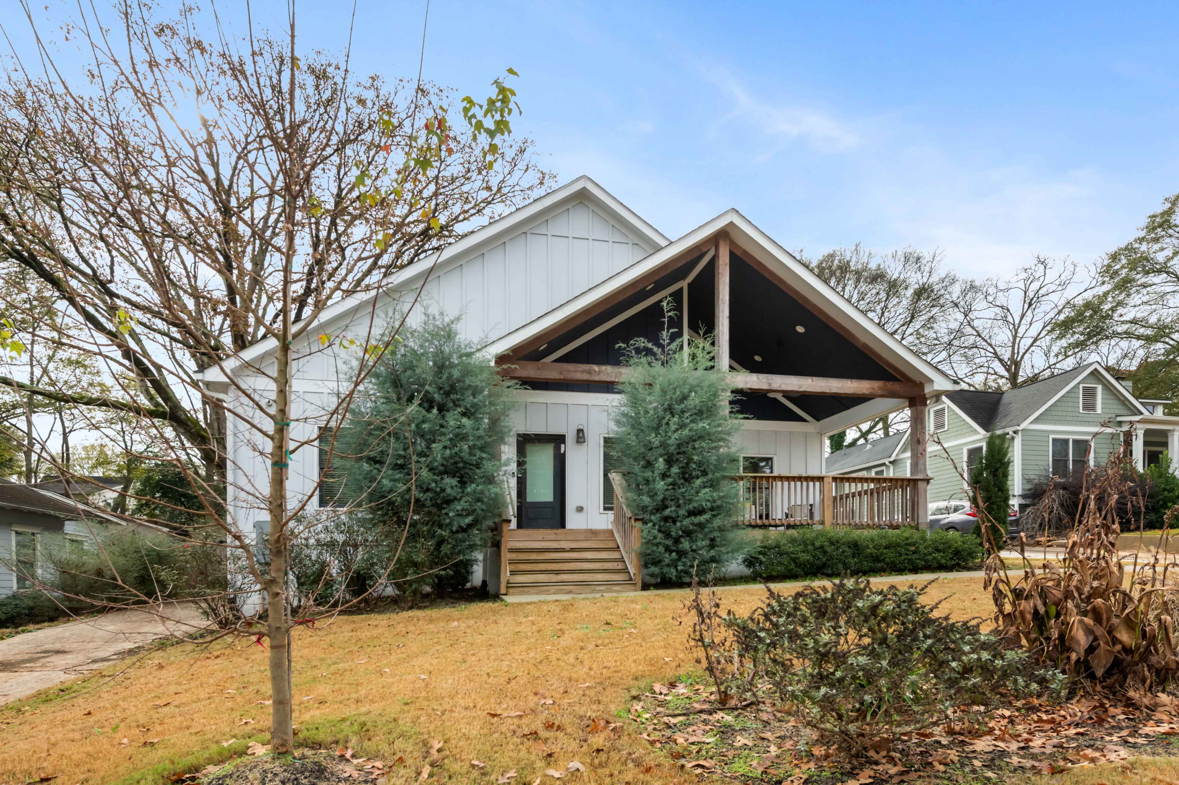 The image shows a modern, single-story house with a front porch and large gabled roof, surrounded by a well-maintained lawn and shrubs.