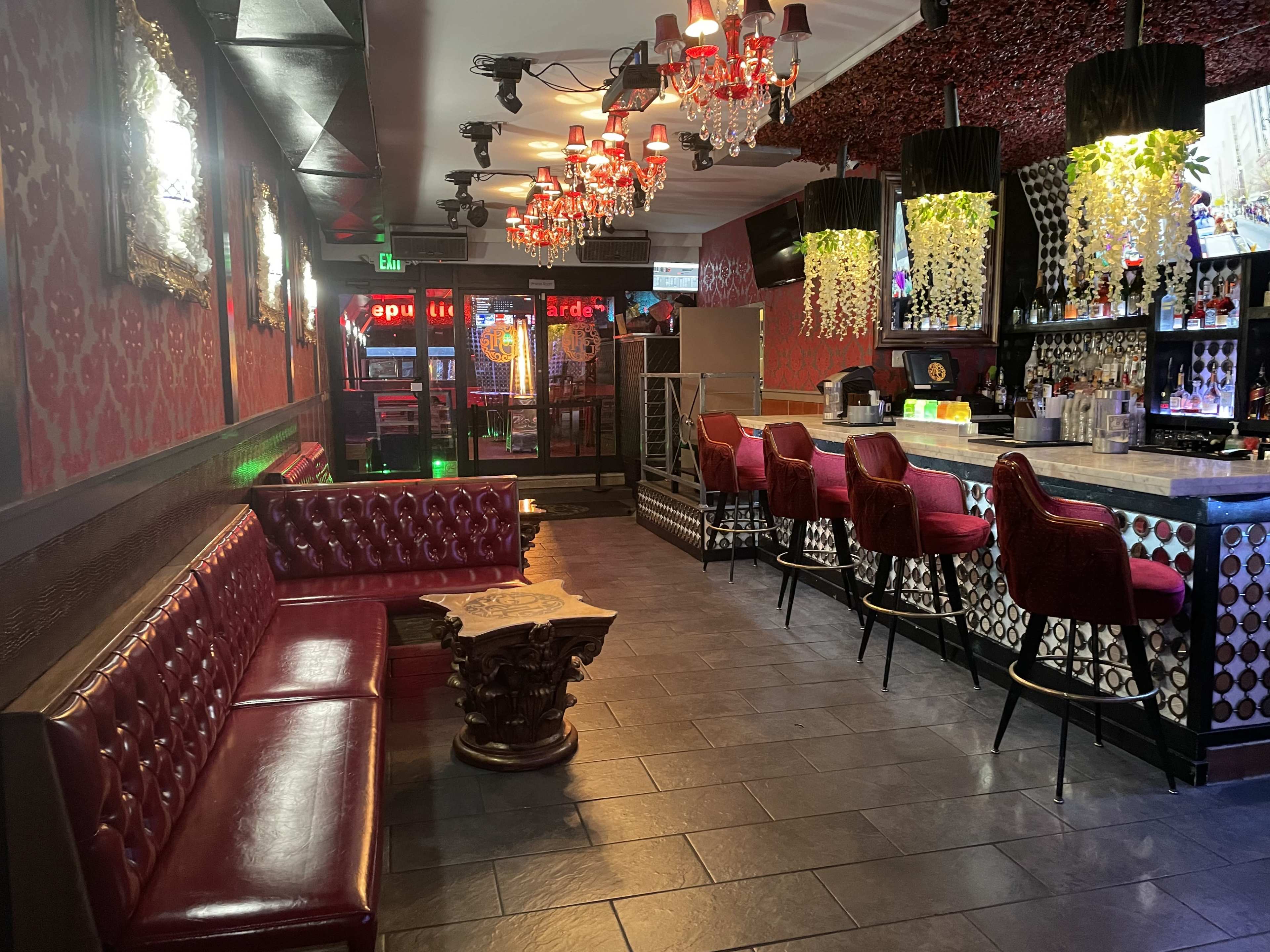 The interior of a bar with red leather seating, a dark tiled floor, and illuminated chandeliers hanging overhead.