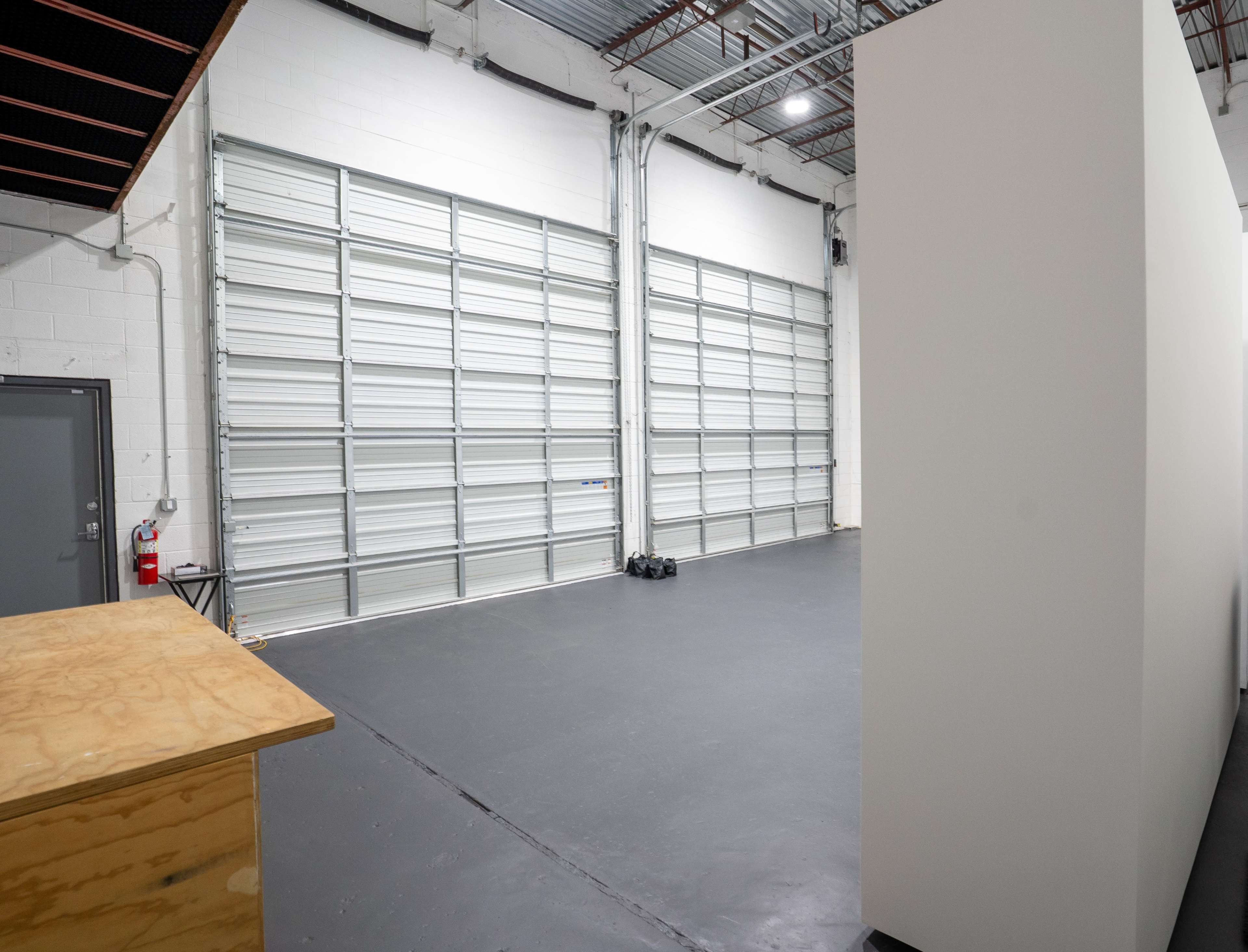 The image shows a spacious, empty industrial area with large garage doors and a blank wall.